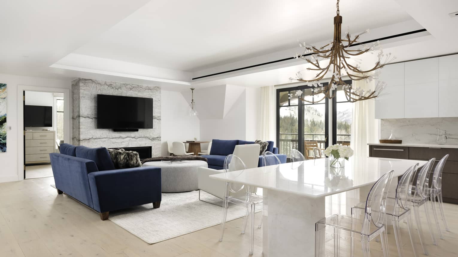 Living area with two dark blue sofas, fireplace, TV, opening to dining area with white table and 8 clear chairs