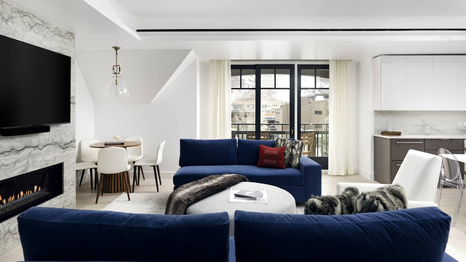 Living room with two dark blue sofas, fireplace, flat-screen TV, windows, white walls