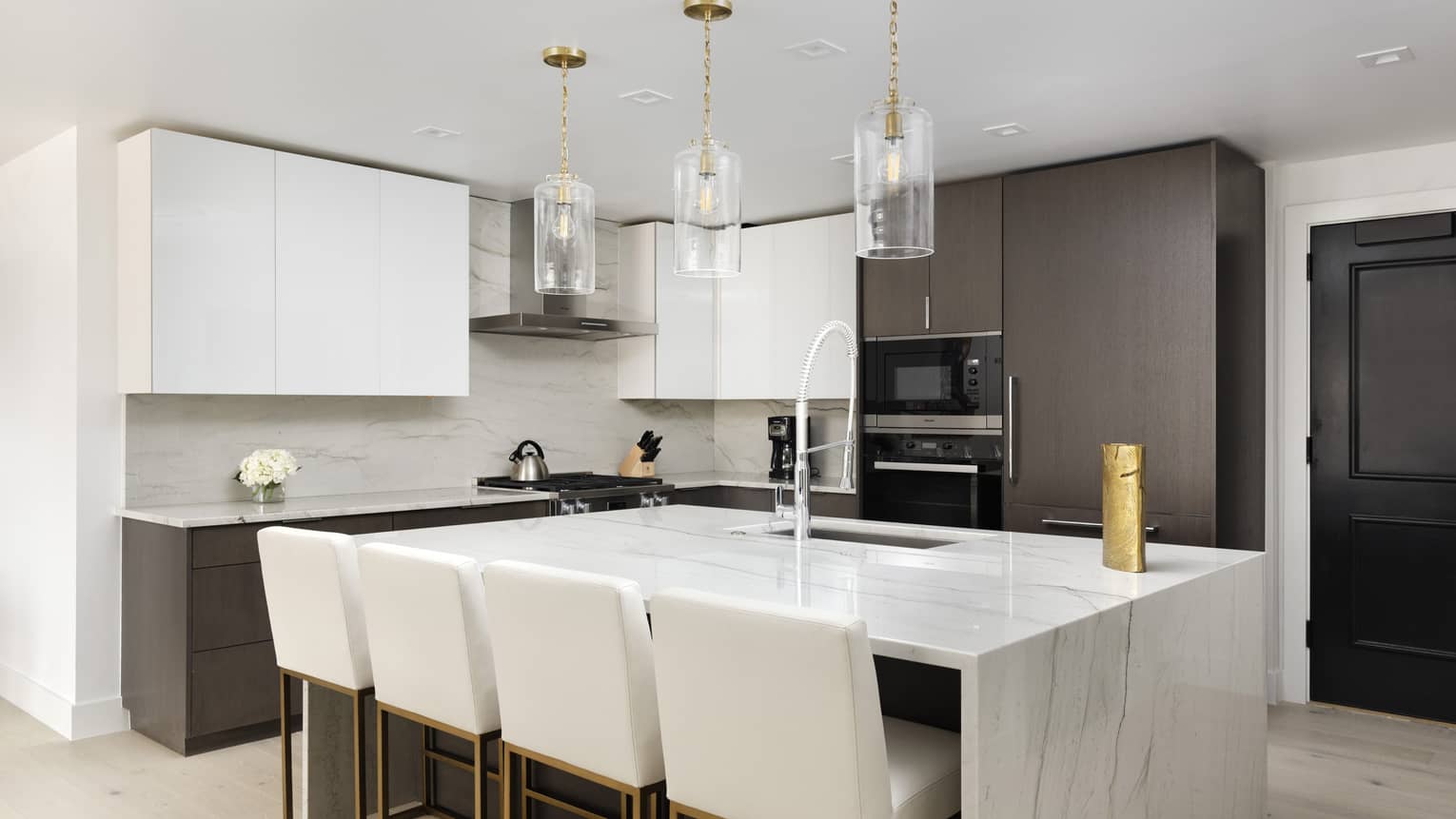 Kitchen with white marble island, four white counter-height chairs, three glass pendant lights