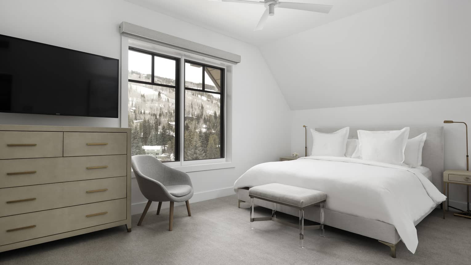 Bedroom with white walls, white king bed, light grey chair, dresser, window