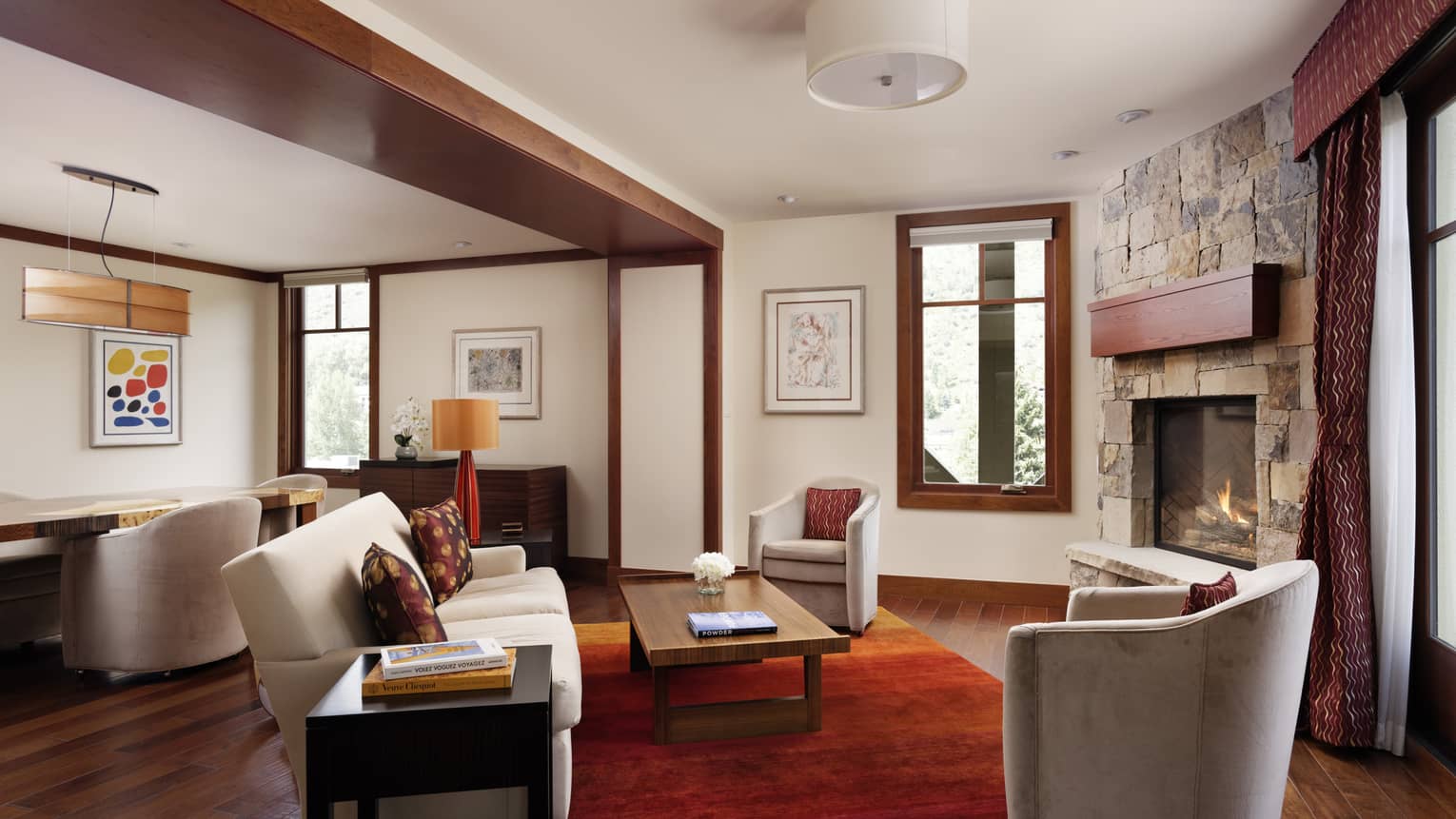 Living room with sofa, rich wooden floors, red area rug, fireplace, two grey armchairs