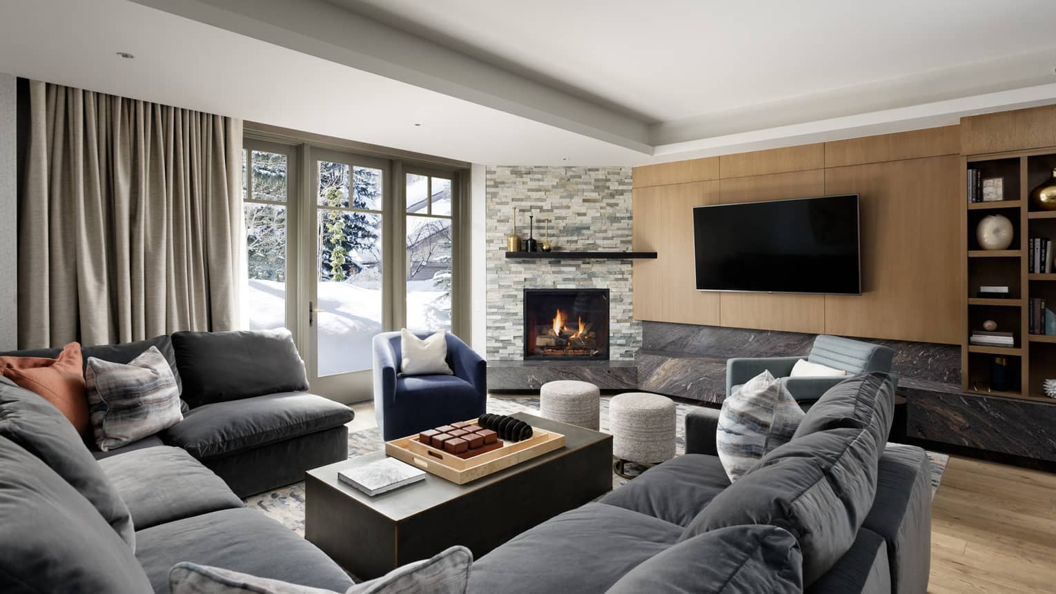 Large grey sectional sofa, wooden floors and walls, TV, fireplace, french doors to outside