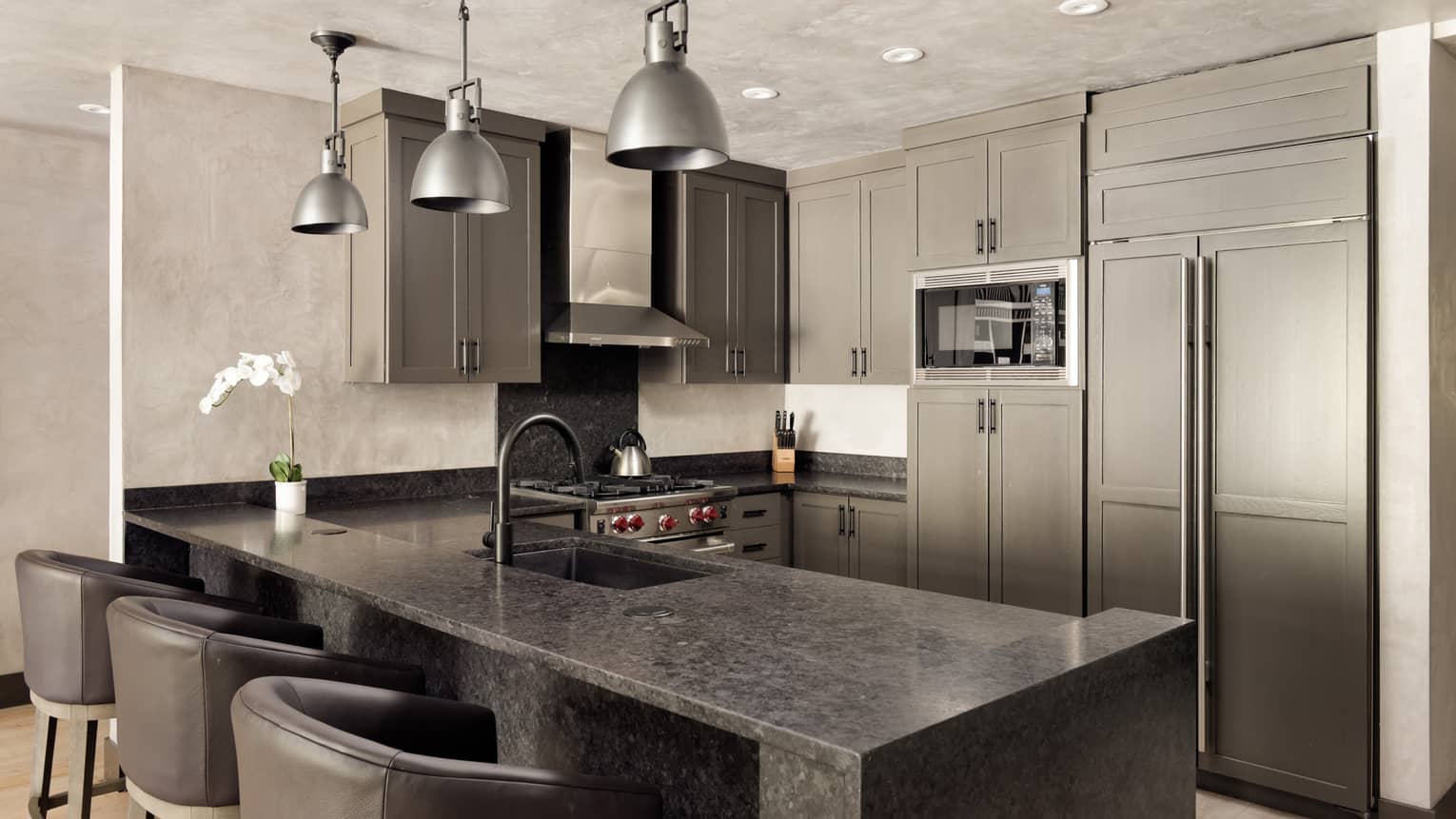 Kitchen with grey cabinets, three metal, hanging lights, three leather counter chairs