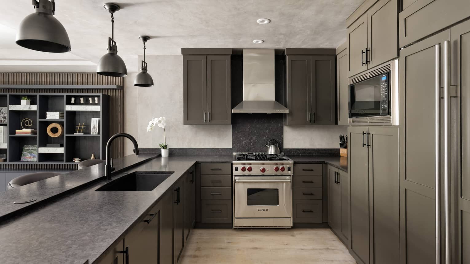 Kitchen with dark grey cabinets, three hanging metal lights, light wood floors