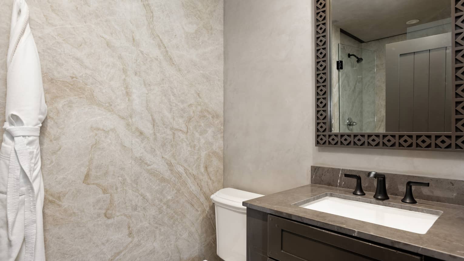 Bathroom with granite wall, white bathrobe on hook, toilet, vanity and mirror