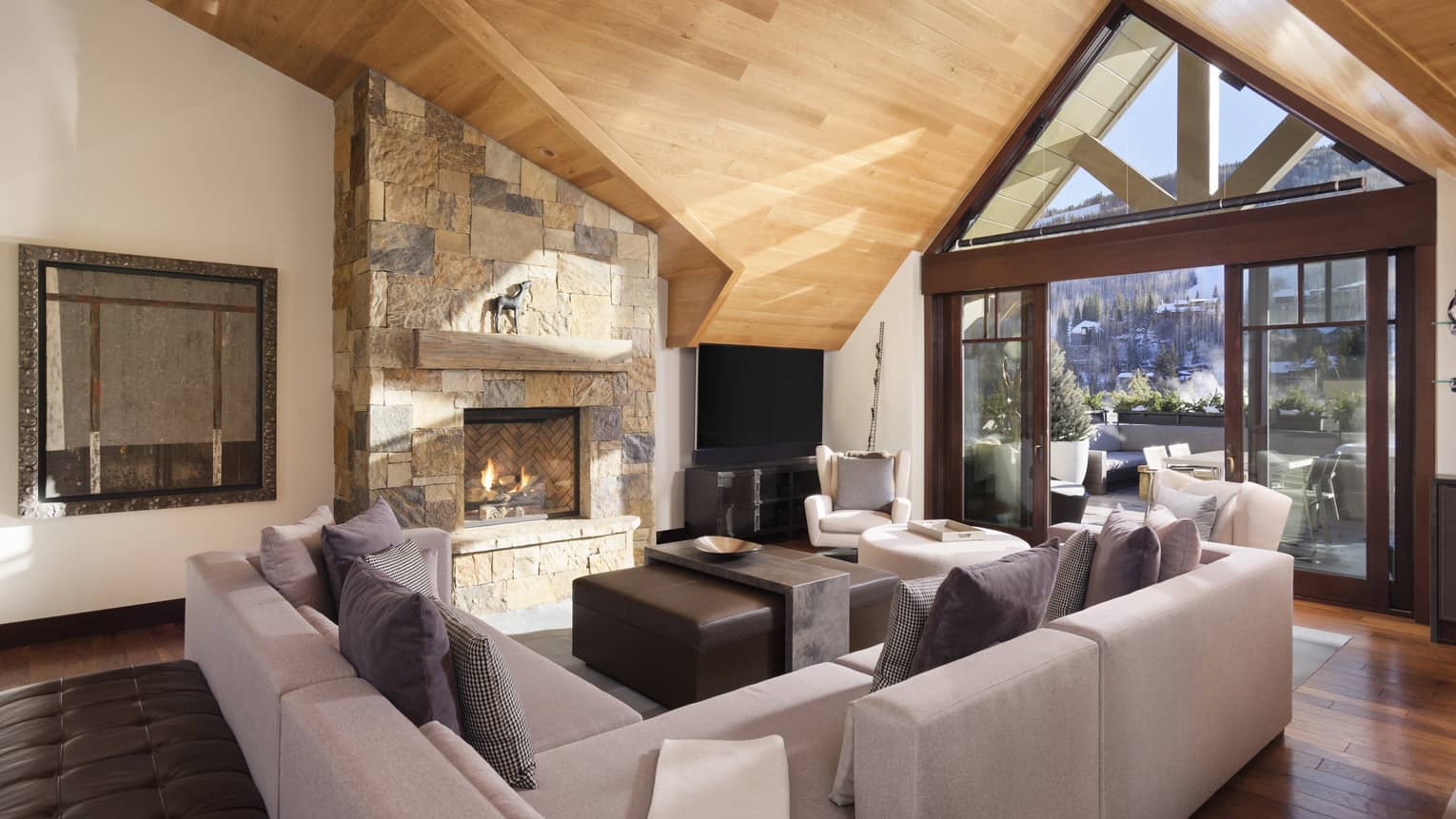 Living room with grey sectional, wooden vaulted ceiling, large window, stone hearth
