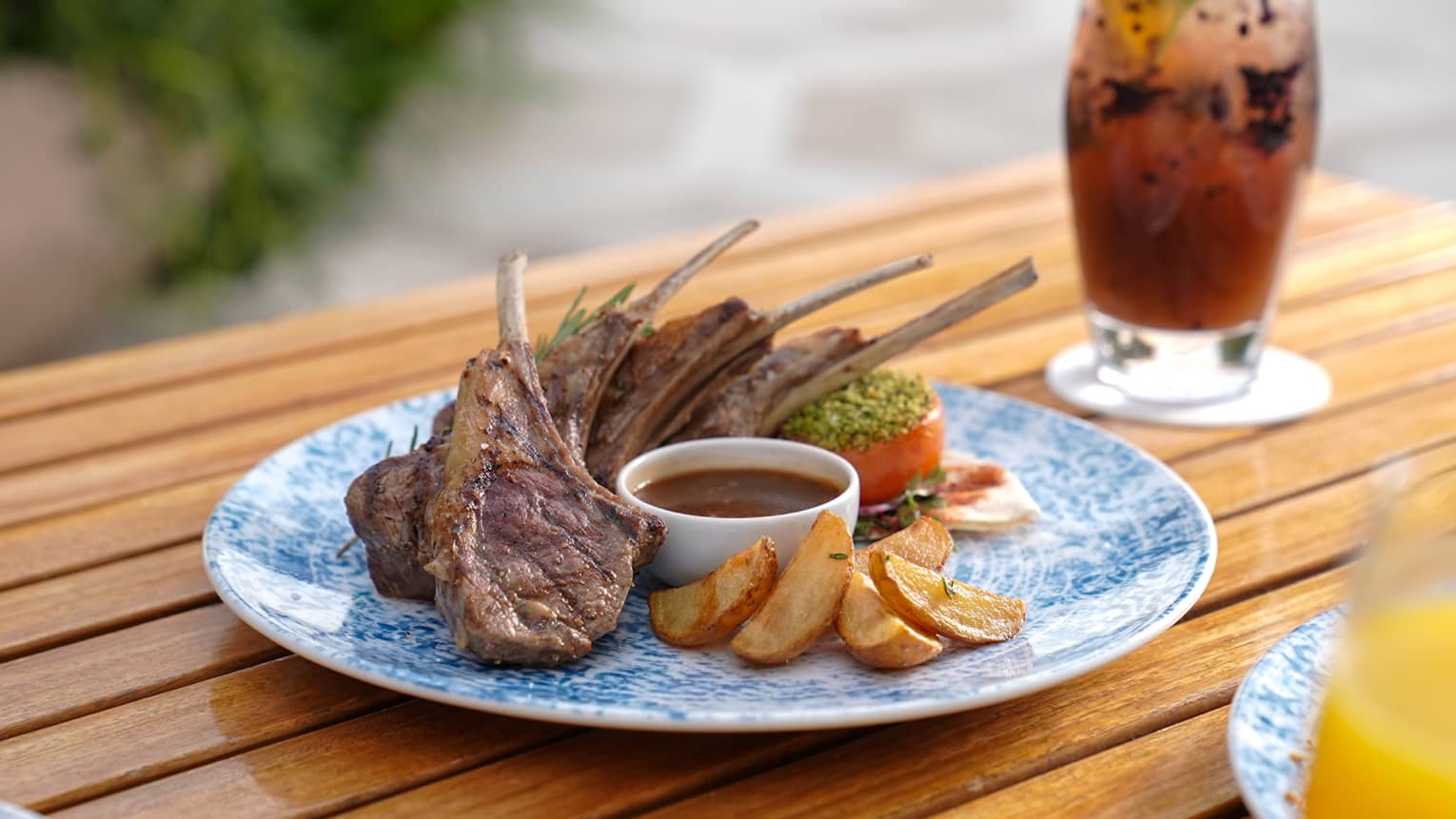 Lamb chops on a plate next to a cocktail.