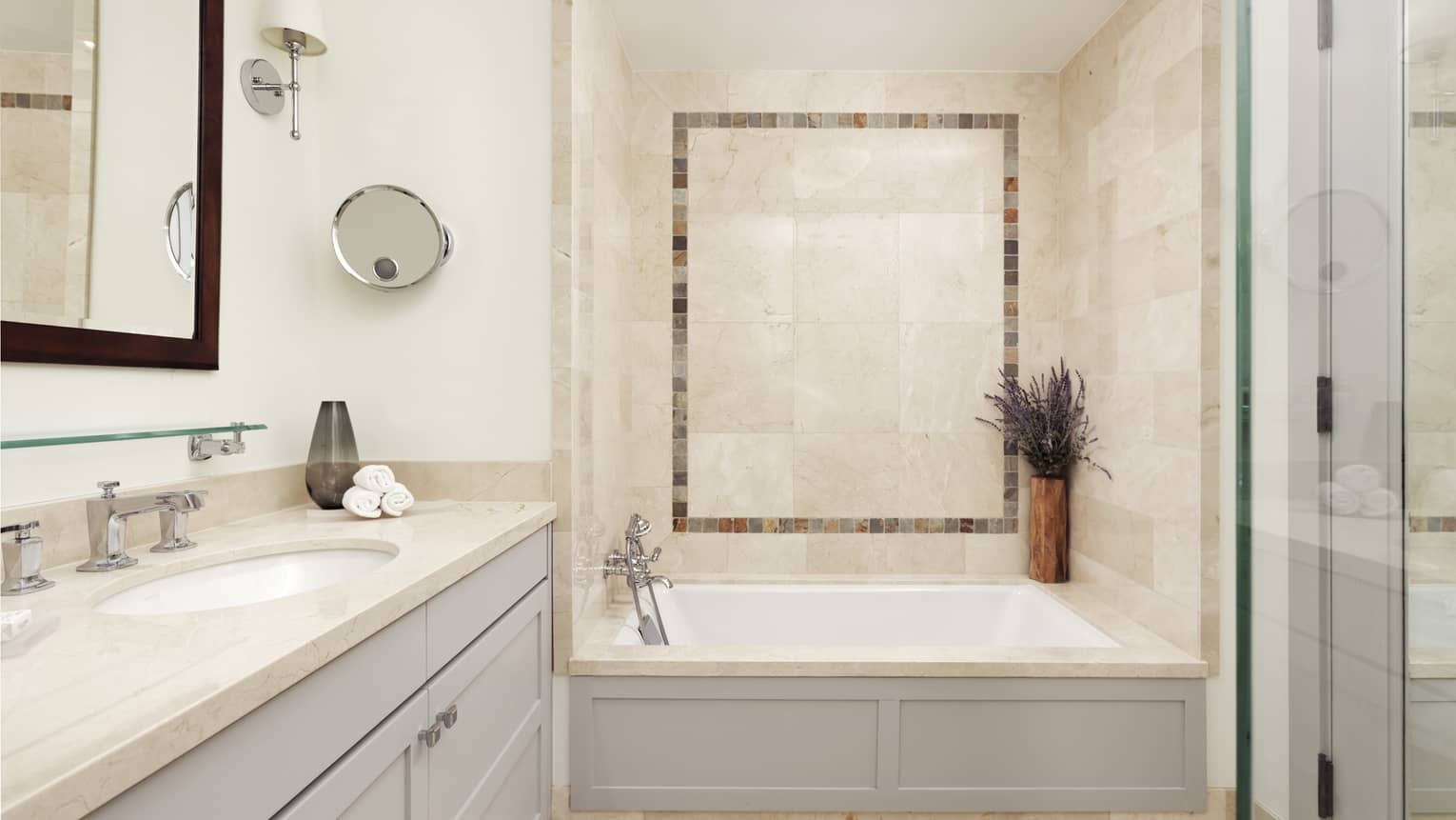 A private Vail residence bathroom has a white stone tile shower with a white porcelain tub and a glass walk-in shower
