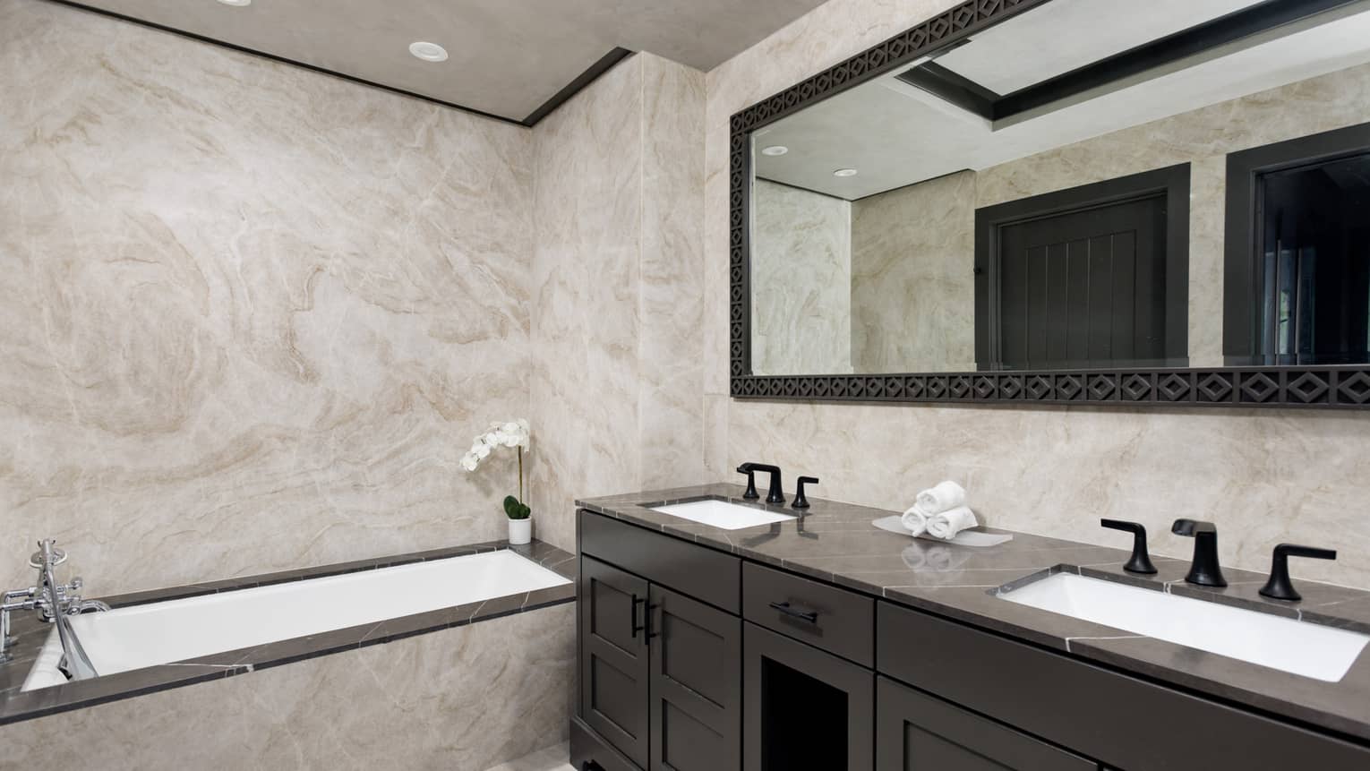 Bathroom with granite walls, built-in tub, double vanity, large mirror