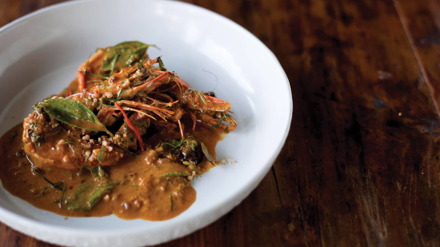 Traditional southern Thai curry dish with head- and tail-on prawns and makrut lime leaves in shallow white bowl