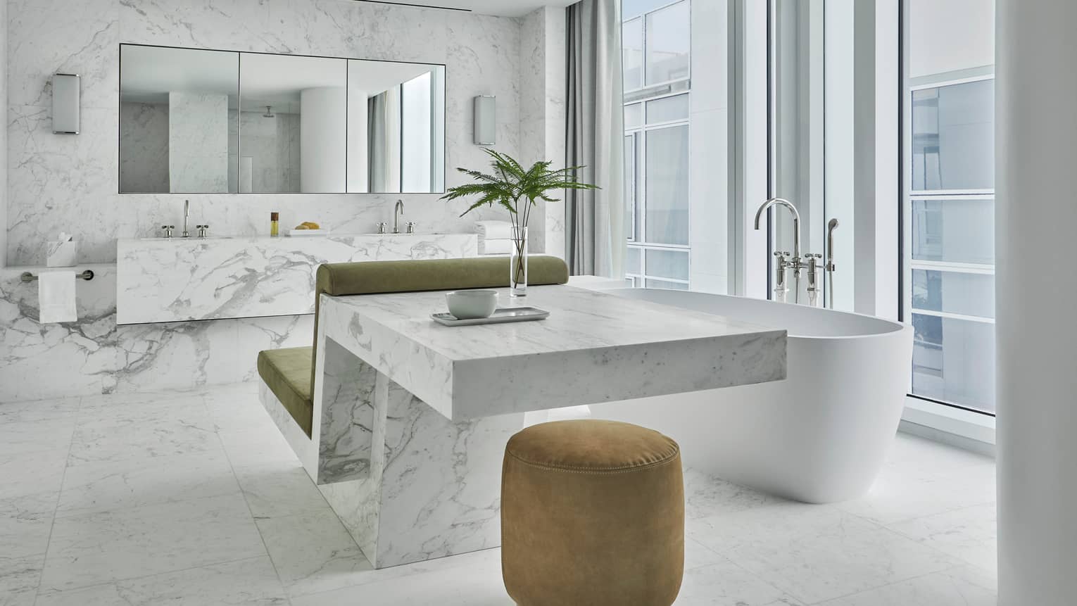 Large, modern white marble bathroom with vanity and sink, plush chair against counter, velvet bench