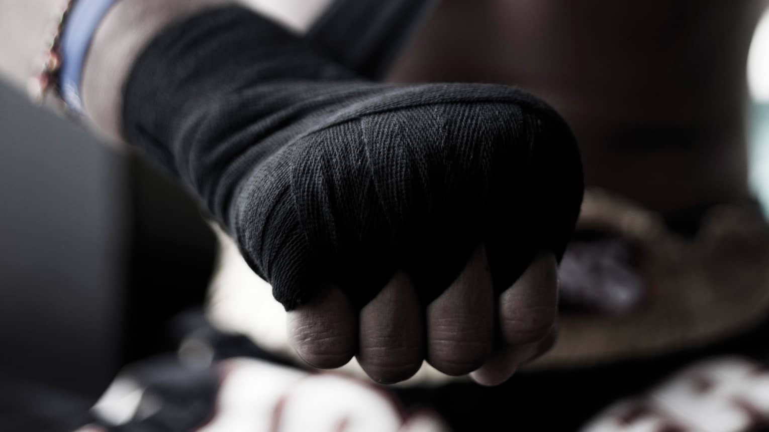 Close-up of a boxer's hand as he winds black fist wrap around his knuckles and wrist to prepare for his lesson.
