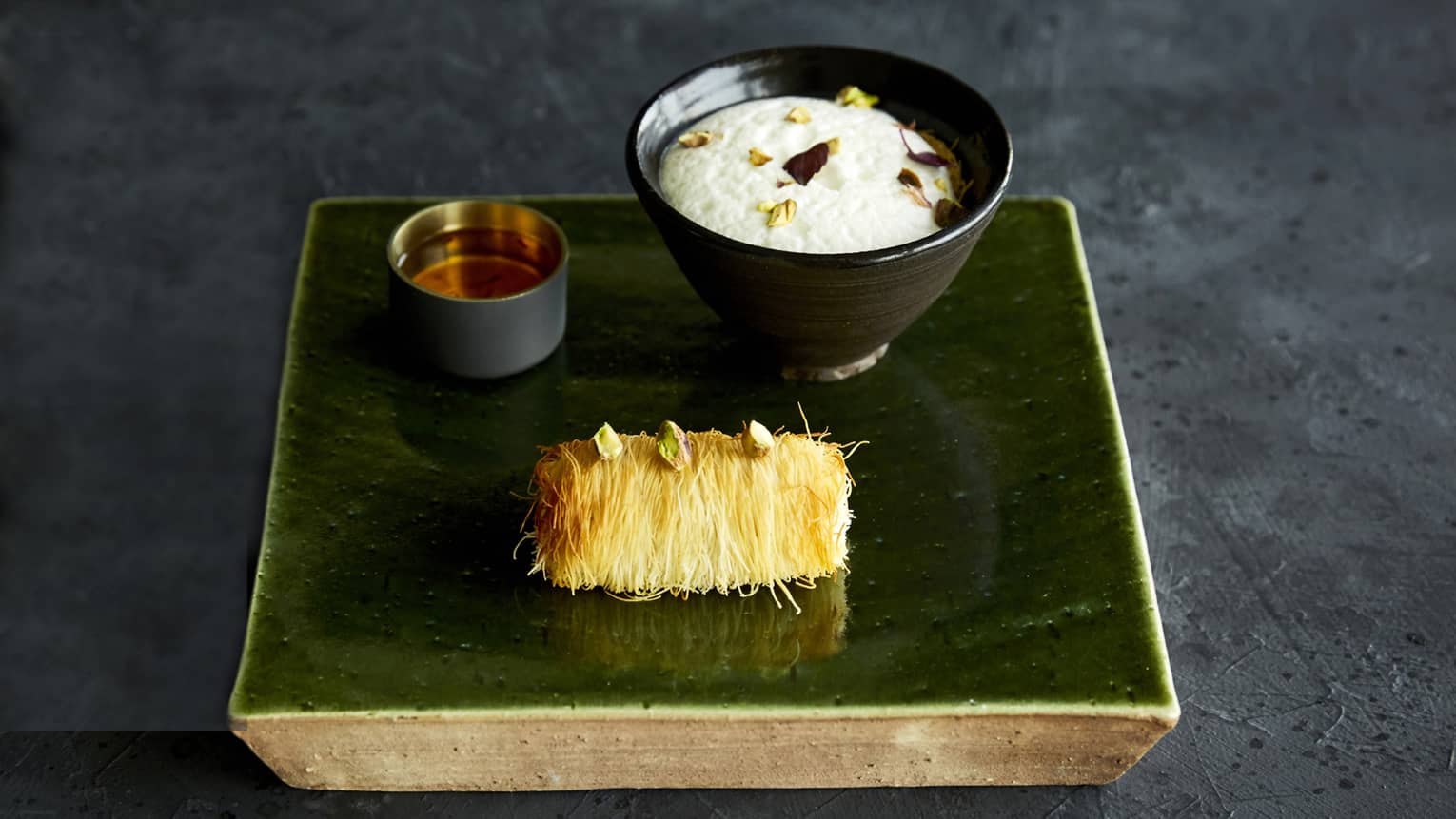 A brass tray holding a single corn on the cobb and white and red dipping sauce