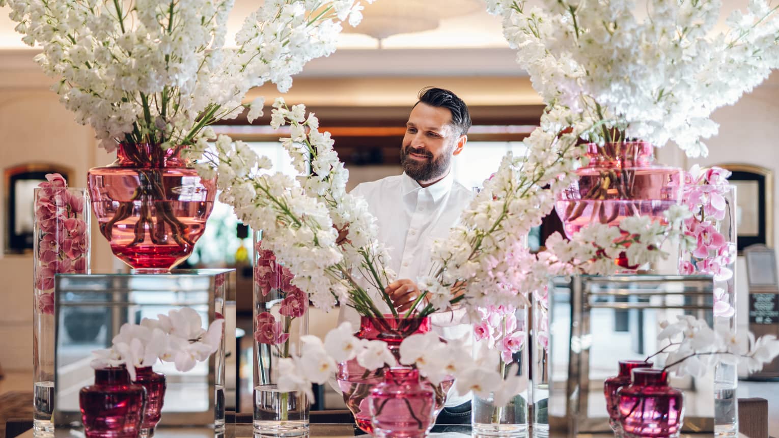 Floral designer standing behind large display of white flower sprays in assorted pink vases