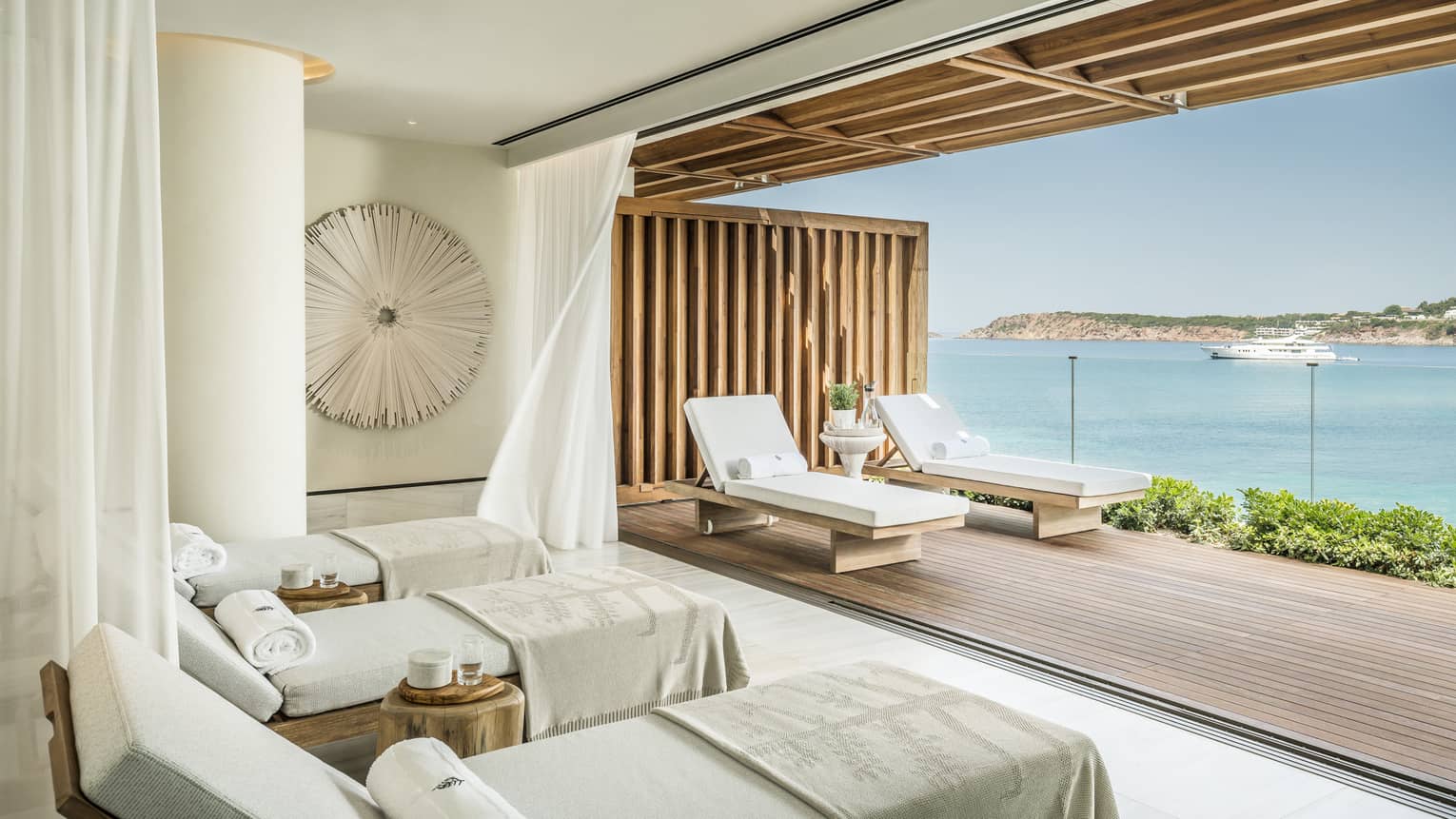 Ocean-facing spa treatment room with reclining treatment beds, towels, overlooking ocean and boat 