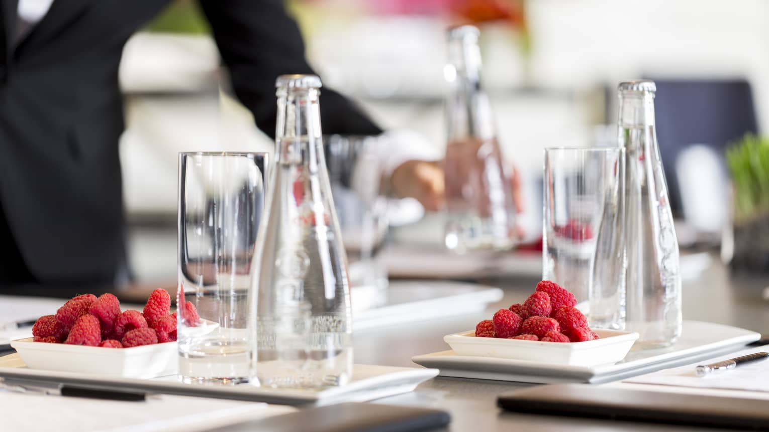 Glass bottles of water and plates of raspberries are set in preparation for a meeting