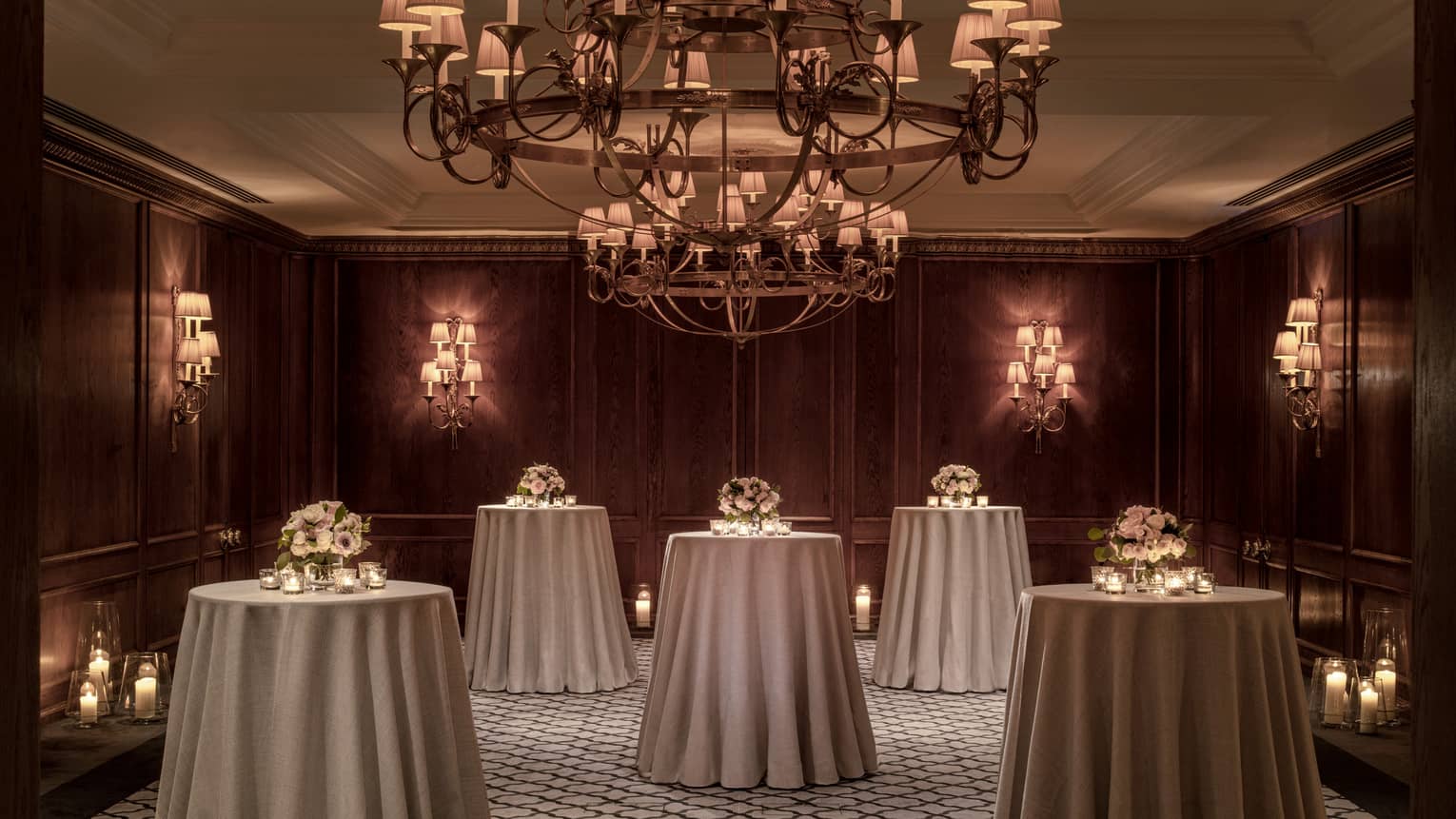 A room with standing round tables and a chandelier.