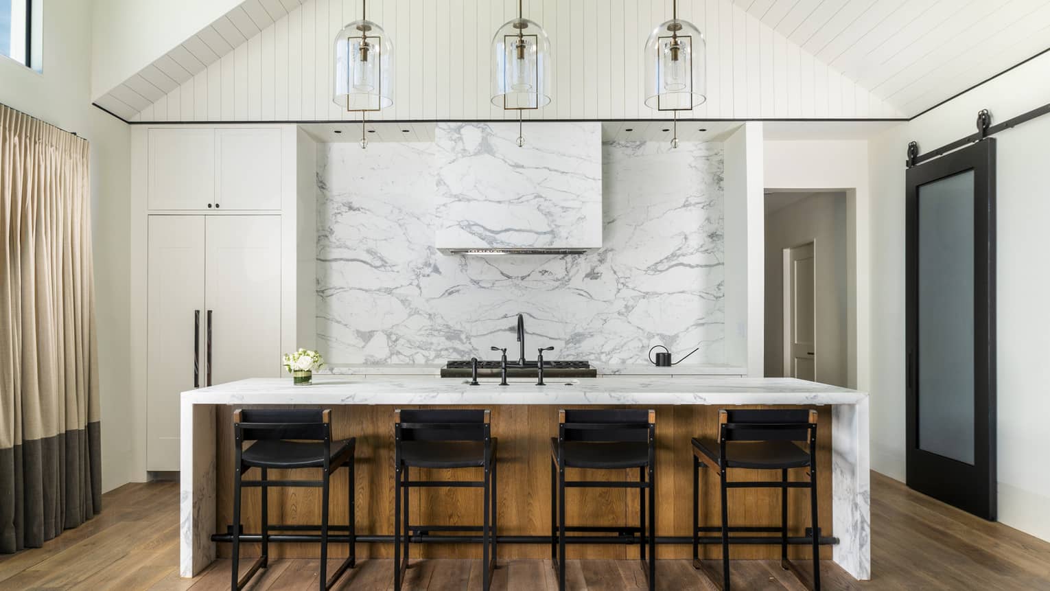 Vaulted ceiling kitchen with marble island and accent wall, four counter-height chairs and three hanging pendant lights