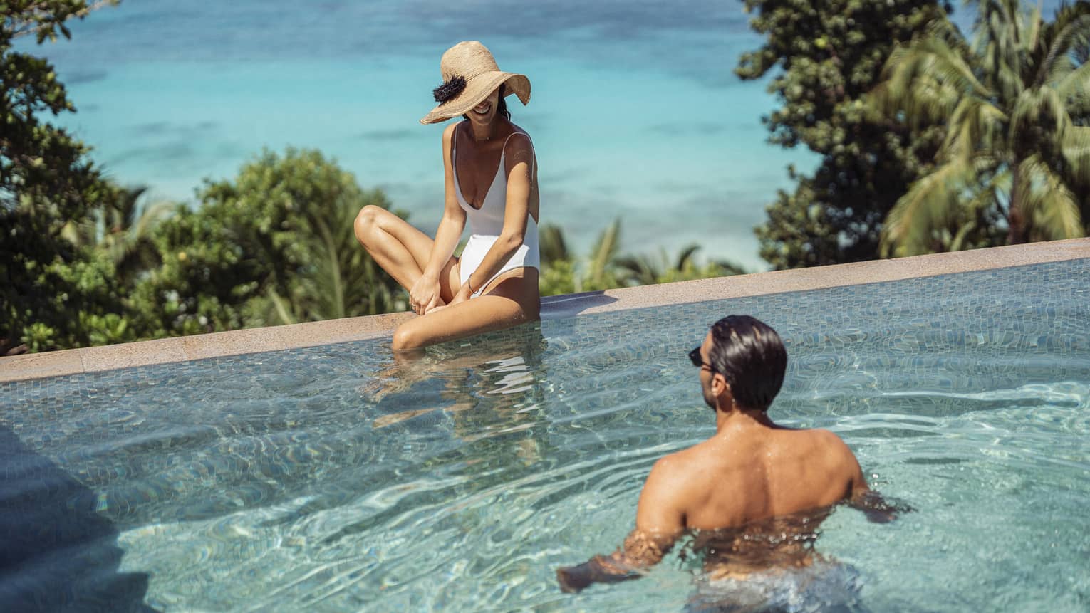 A couple relaxes in an infinity pool overlooking the beach