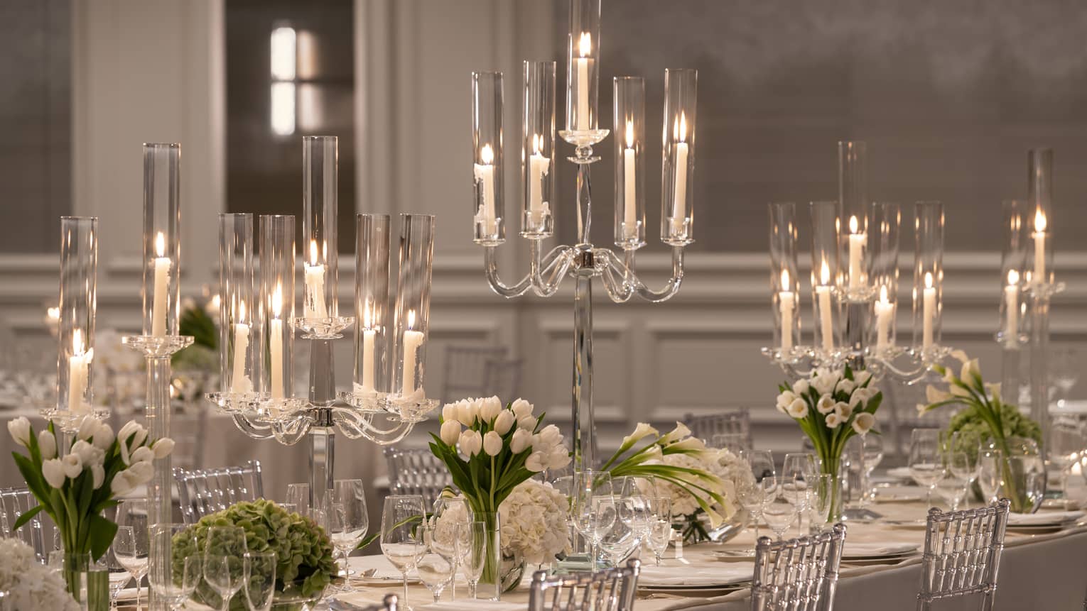 Formally set white dining table with candelabras and white flowers flanked by silver chairs