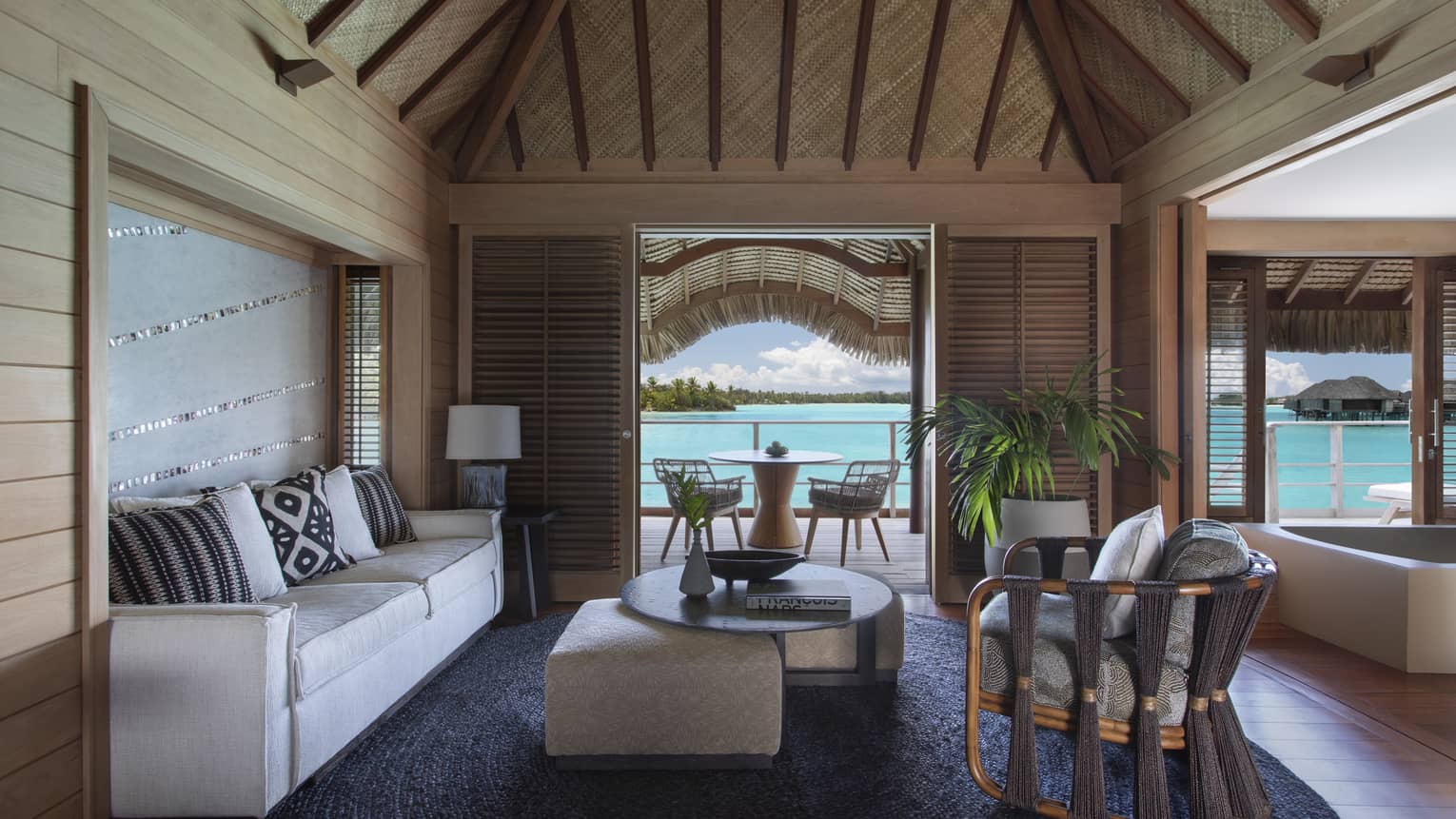 Living room with thatched roof, white sofa, arm chair, coffee table, view of turquoise lagoon
