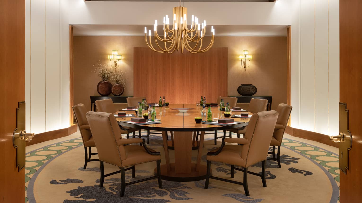 Boardroom with chandelier over circular wooden table and brown leather parsons chairs 