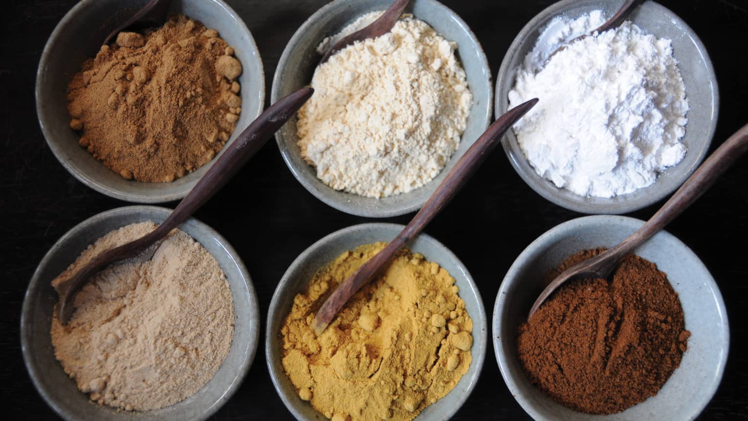 Aerial view of small spa bowls with powdered spices, clays, wood spoons
