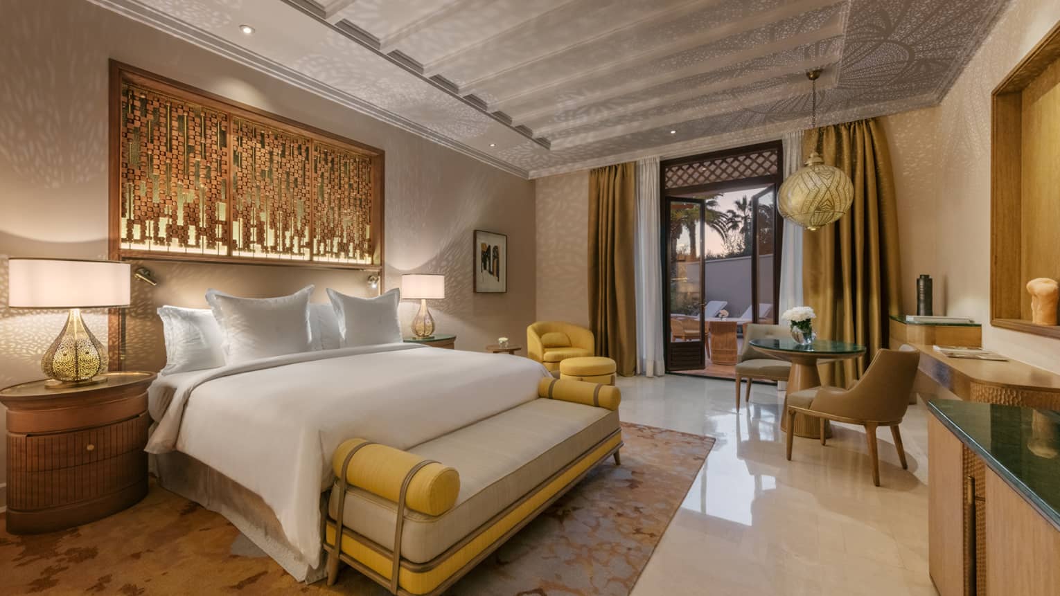 Marrakech hotel room with king bed, cushioned bench, yellow and bronze accents