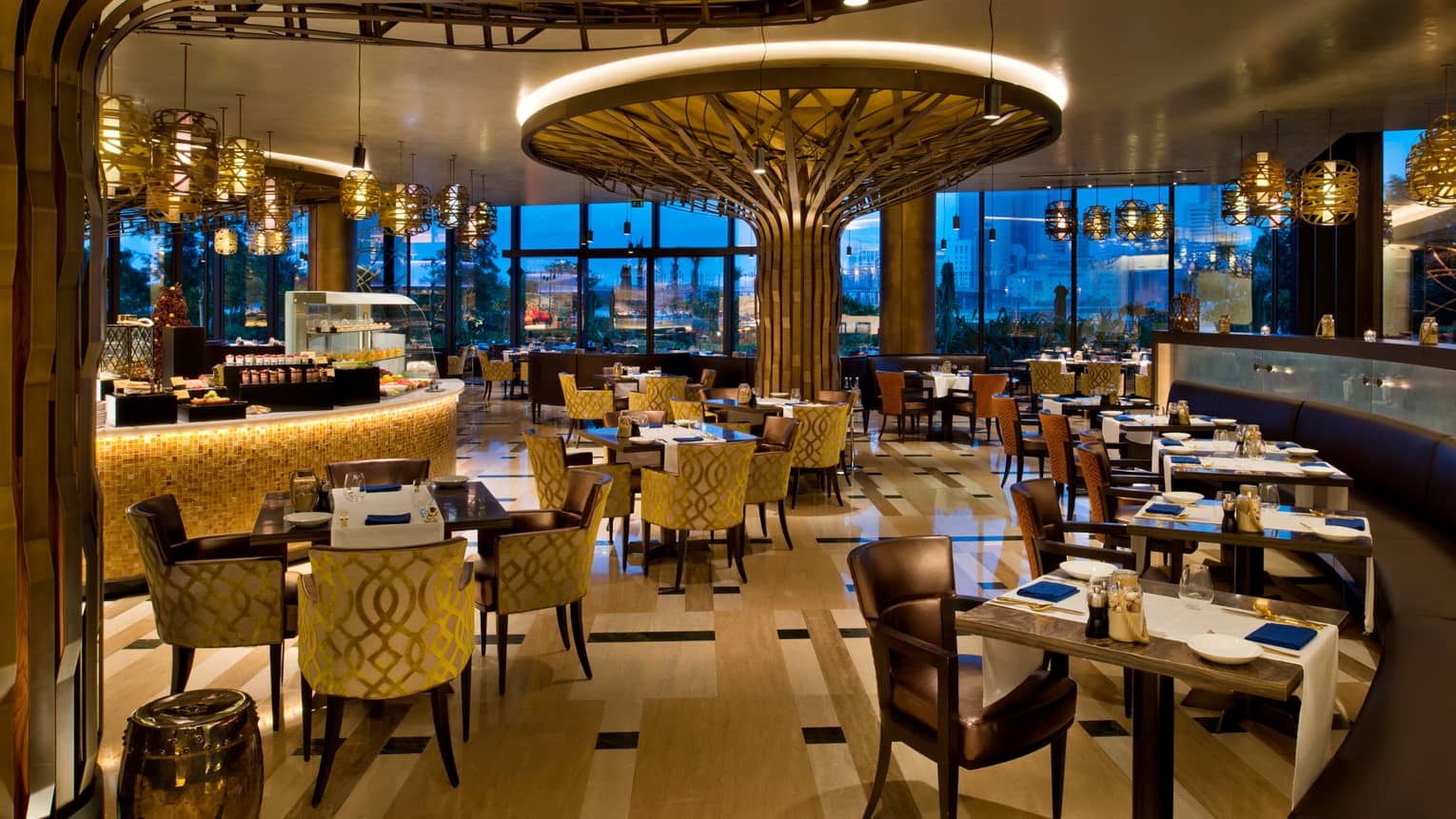 Bahrain Bay Kitchen dimly-lit dining room with gold velvet armchairs, tile bar, tall tree-shaped wood sculpture with light