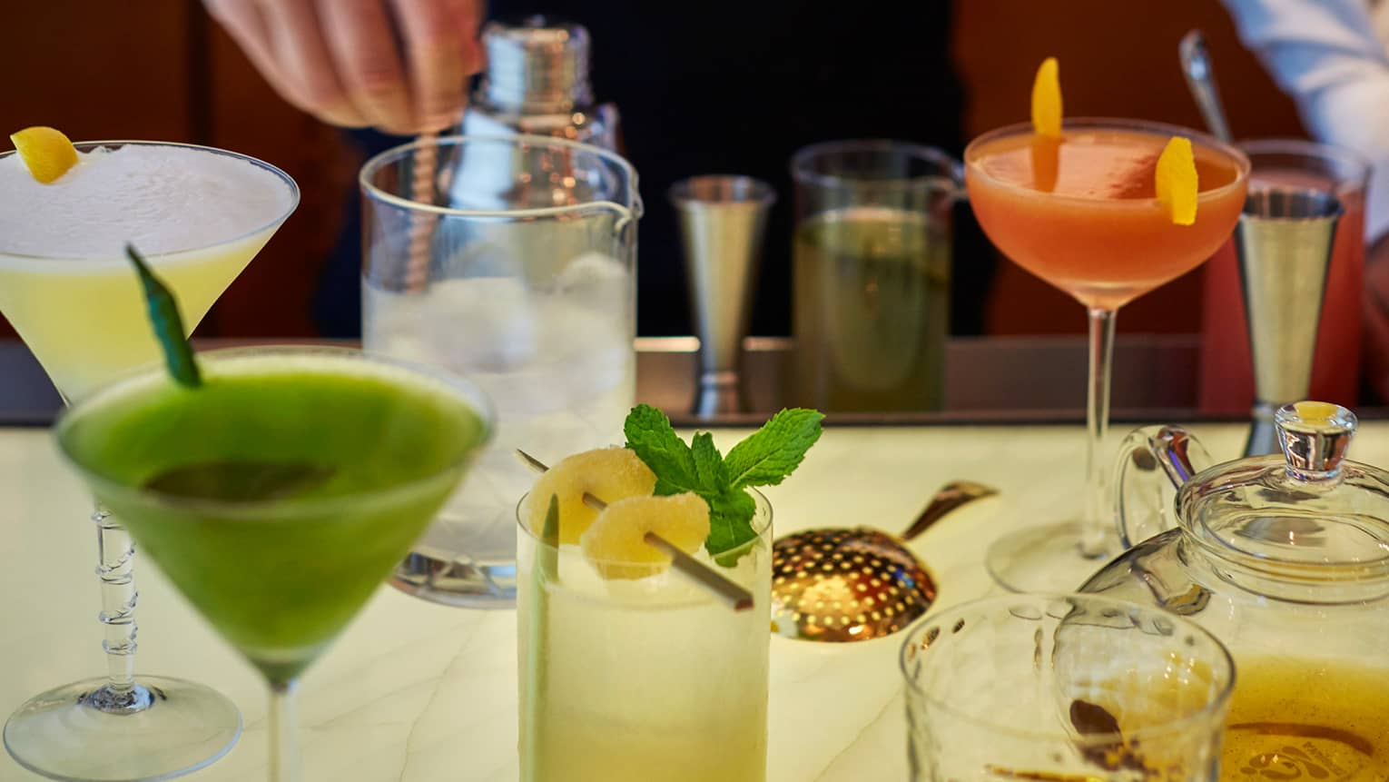 Bartender stirs ice in glass jar, margaritas, cocktails on table