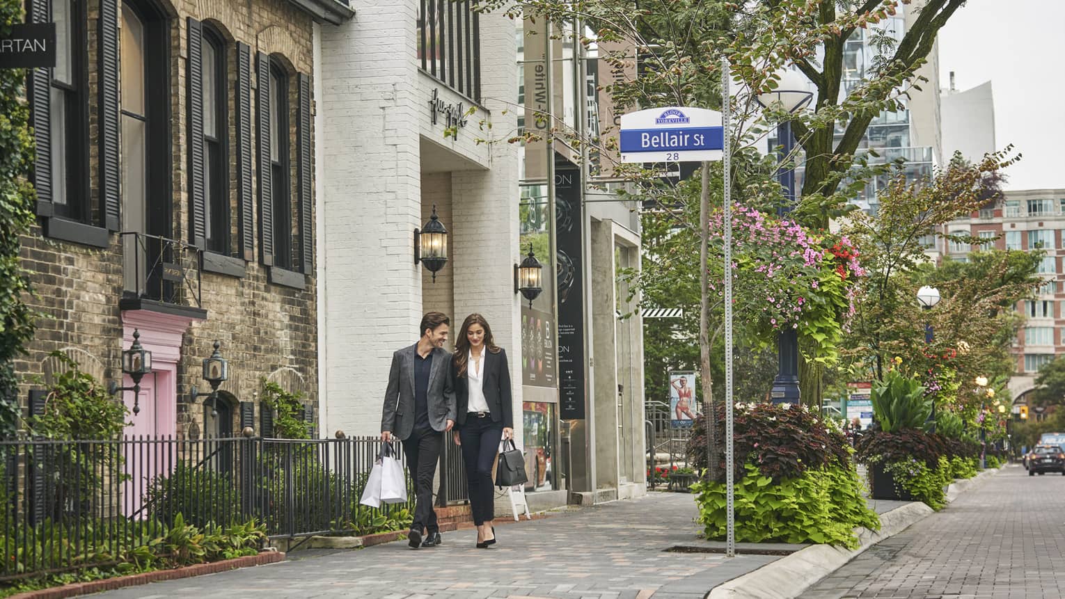 Fashionable couple walk down sidewalk in Toronto's Yorkville shopping district