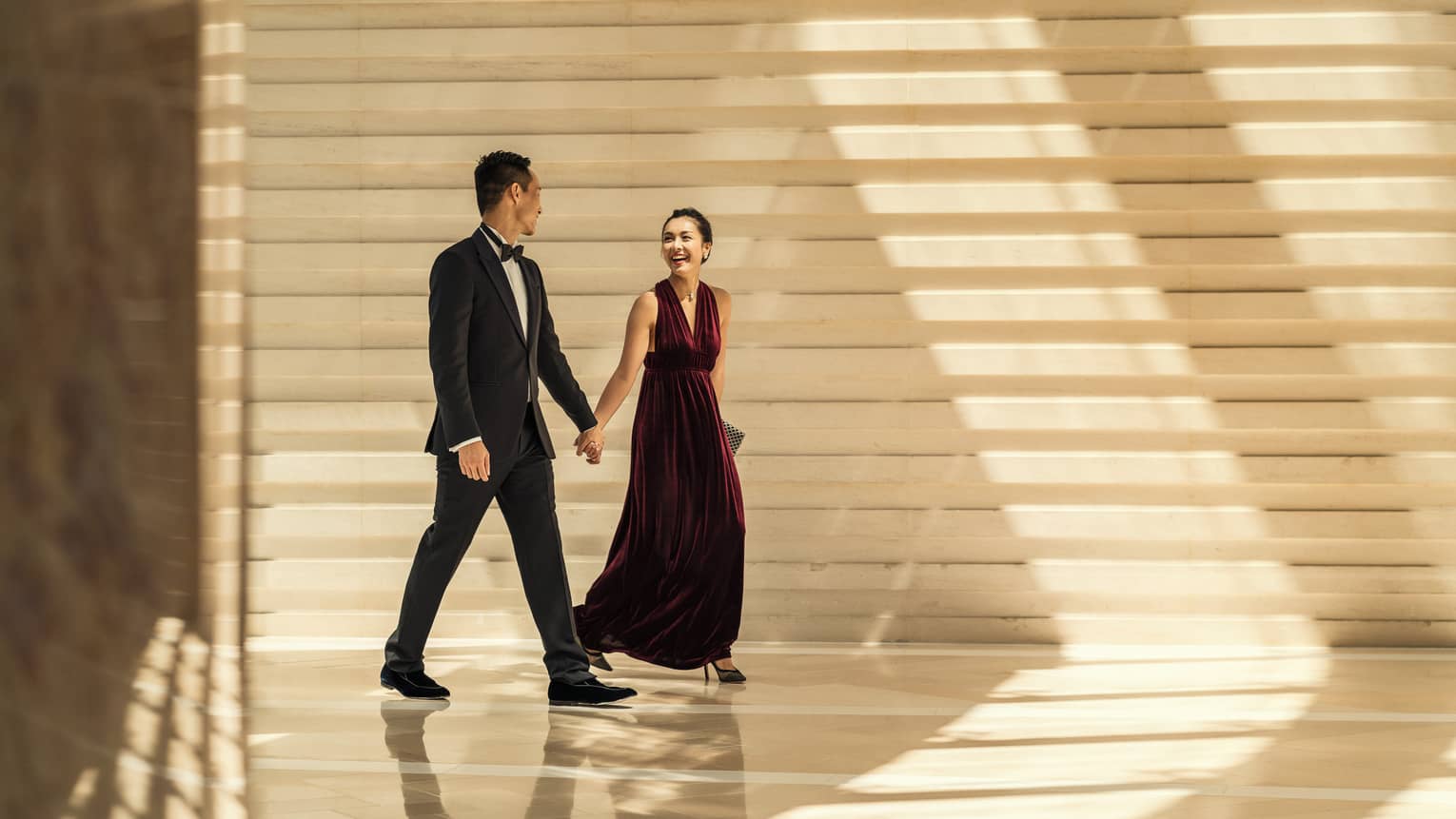 Man and woman in formal wear hold hands at Four Seasons Hotel Hong Kong.