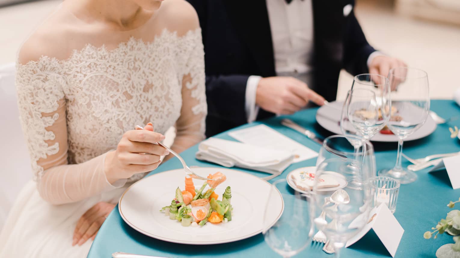 Bride and groom sitting at blue and white formally set table, eating salad
