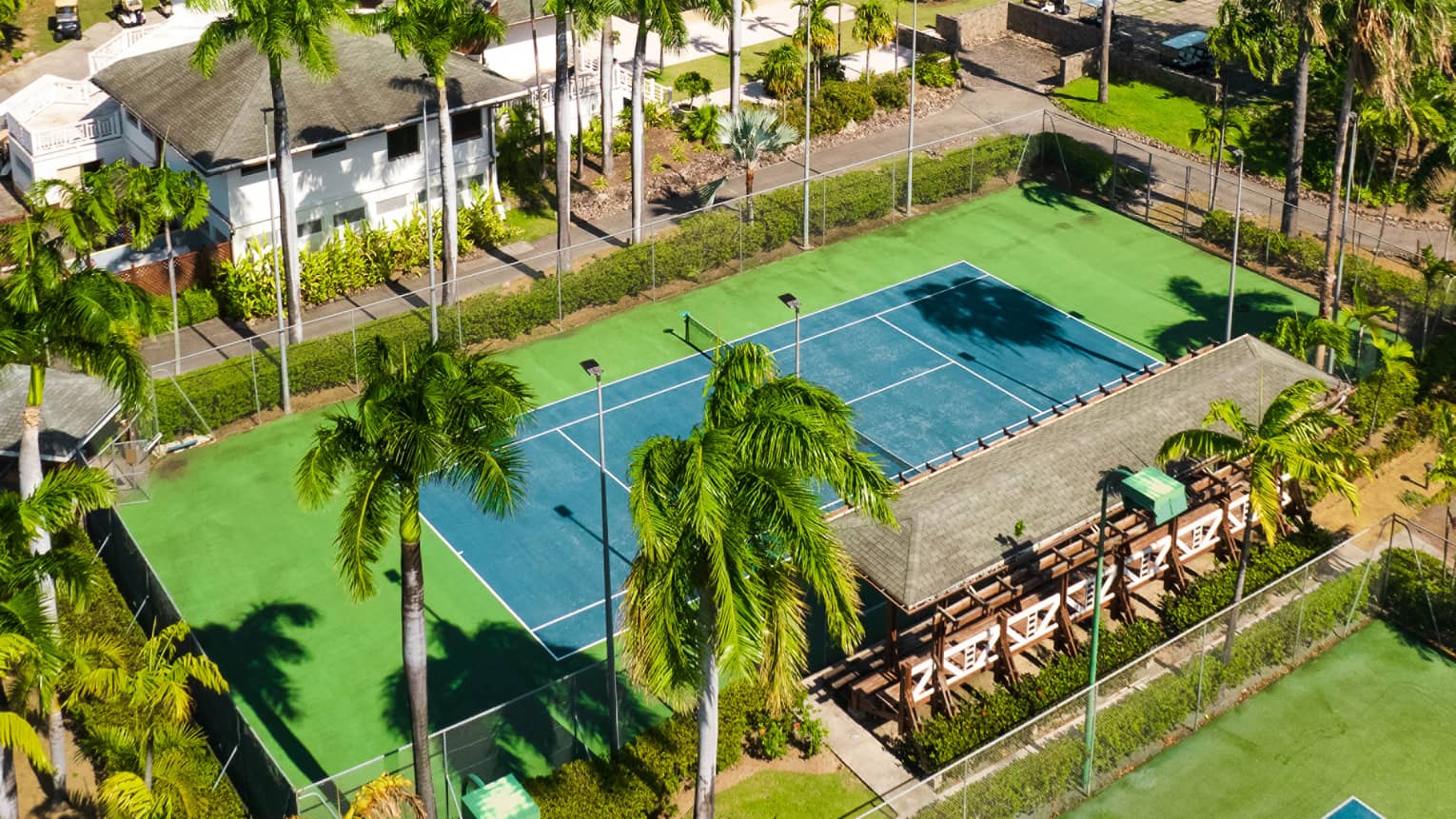 A tennis court surrounded by lush green trees, white building and a mountain in the background.