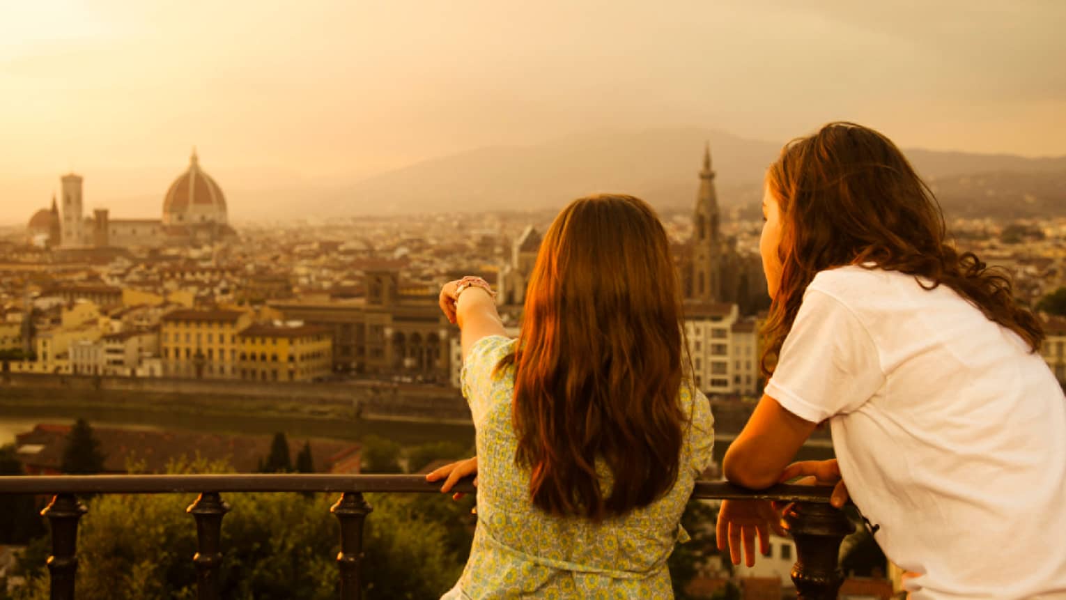 Back of two young girls looking out over Florence skyline, rooftops, Duomo at sunset