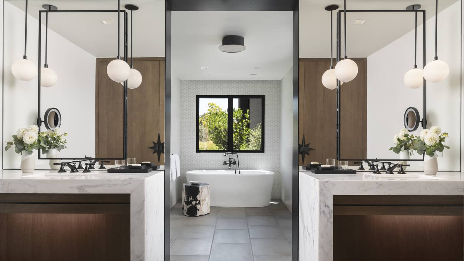 Large bathroom with two marble vanities, tile floor, standalone tub, window