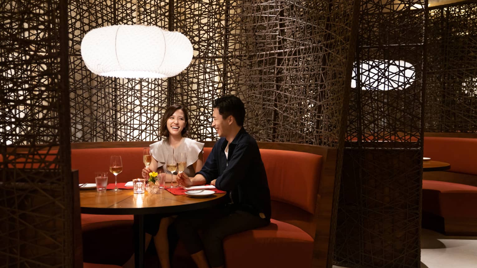 Woman and man smile at each other at rounded booth table in restaurant at Four Seasons Hotel Kyoto