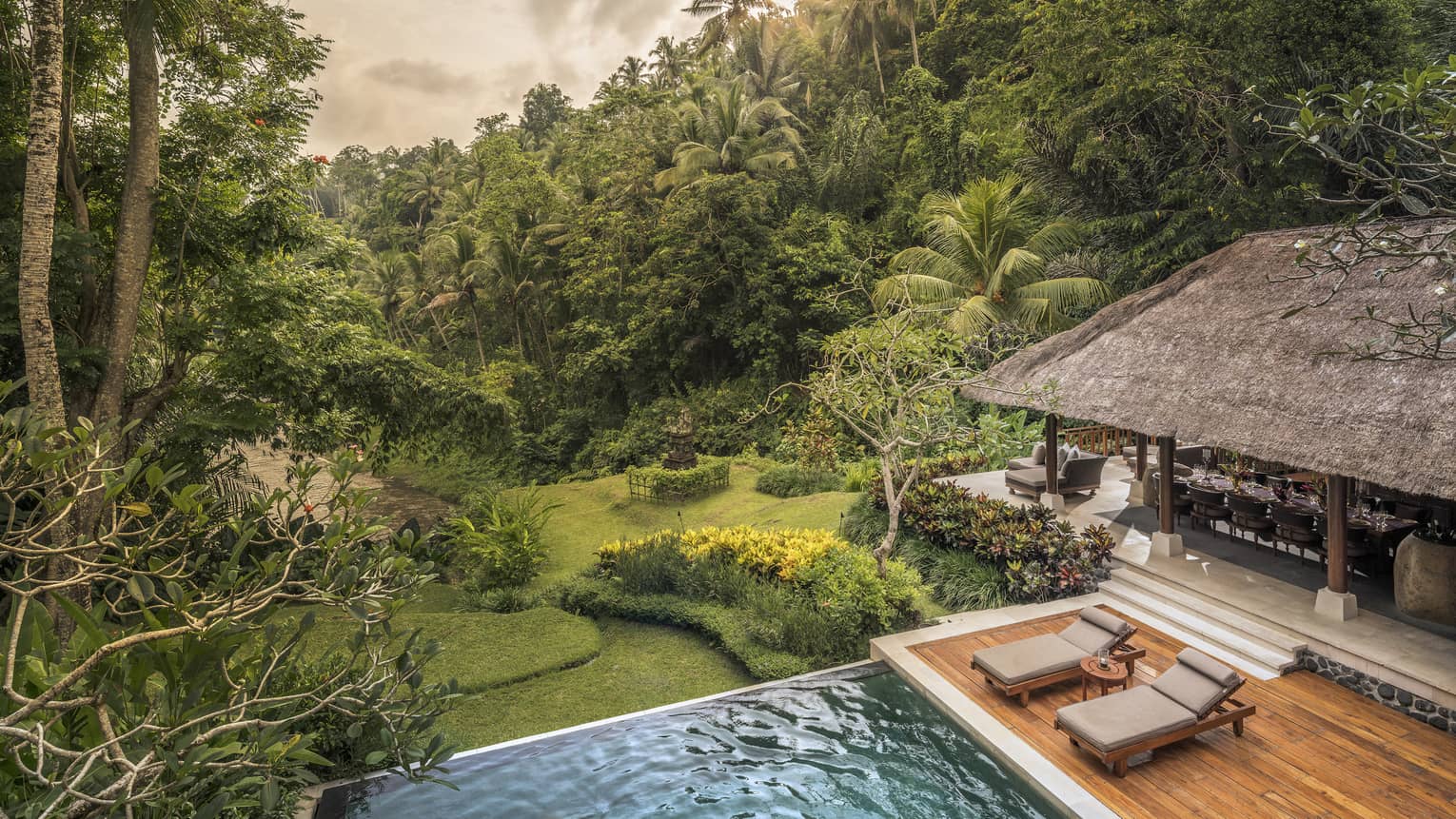 A villa with cushioned chairs and an infinity pool overlooking a river in Bali