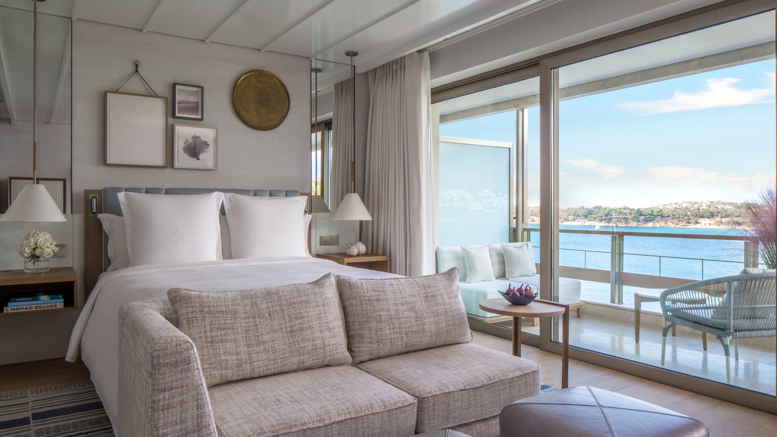 Bedroom with white king bed, sofa at the end of the bed, two square leather ottomans, sliding glass door with sea view