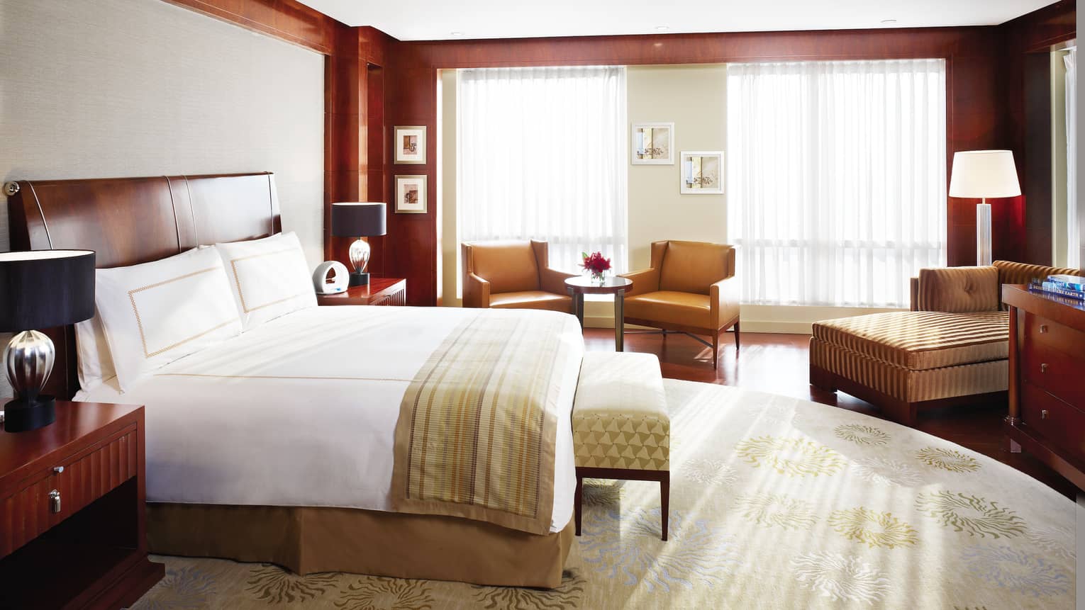 Presidential Suite bed, striped blanket, bench, brown leather armchairs and chaise by window