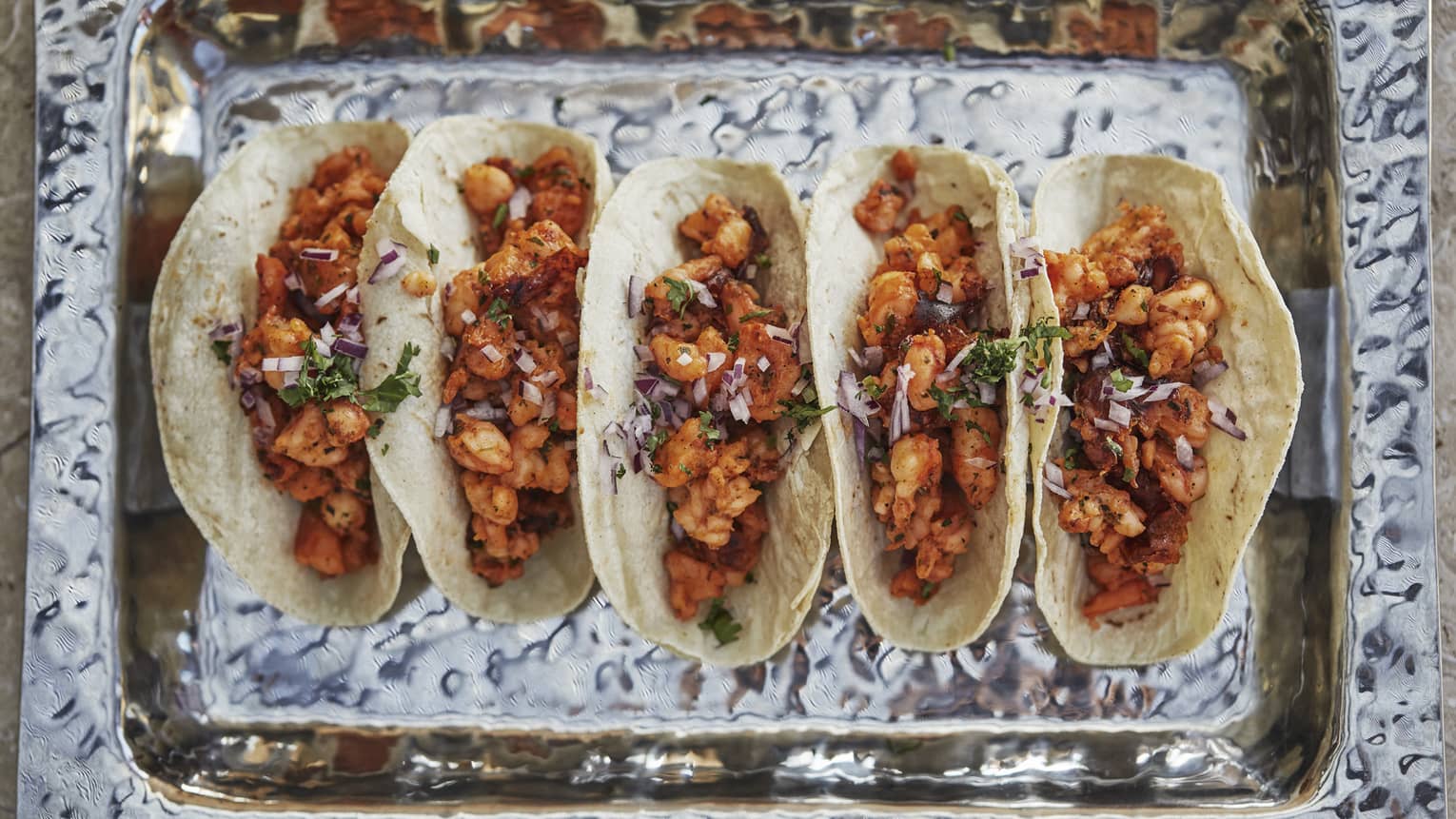 Aerial view of row of five tacos in dish