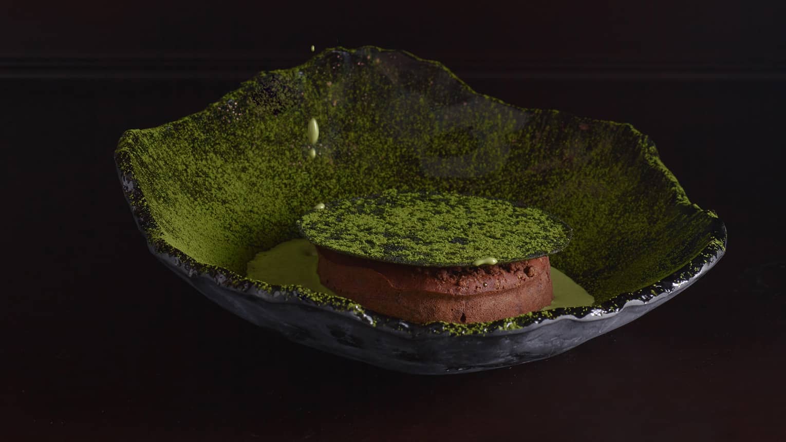 Round Chocolate Lava Cake with Matcha Cap in green ceramic raw-edged bowl with Matcha Sauce being poured over