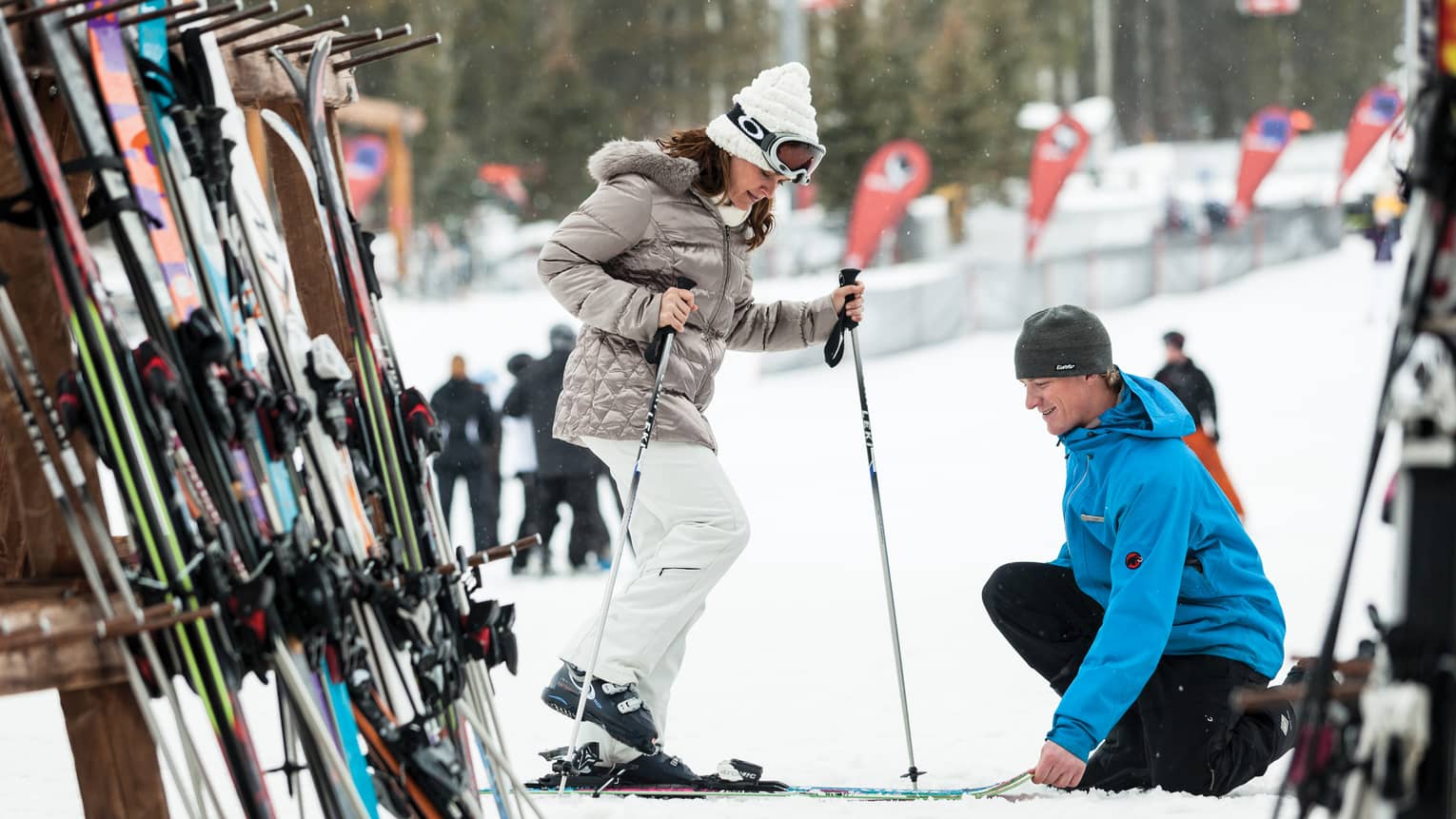 Hotel staff holds skis as woman holding poles steps in by ski rack, snowy hill