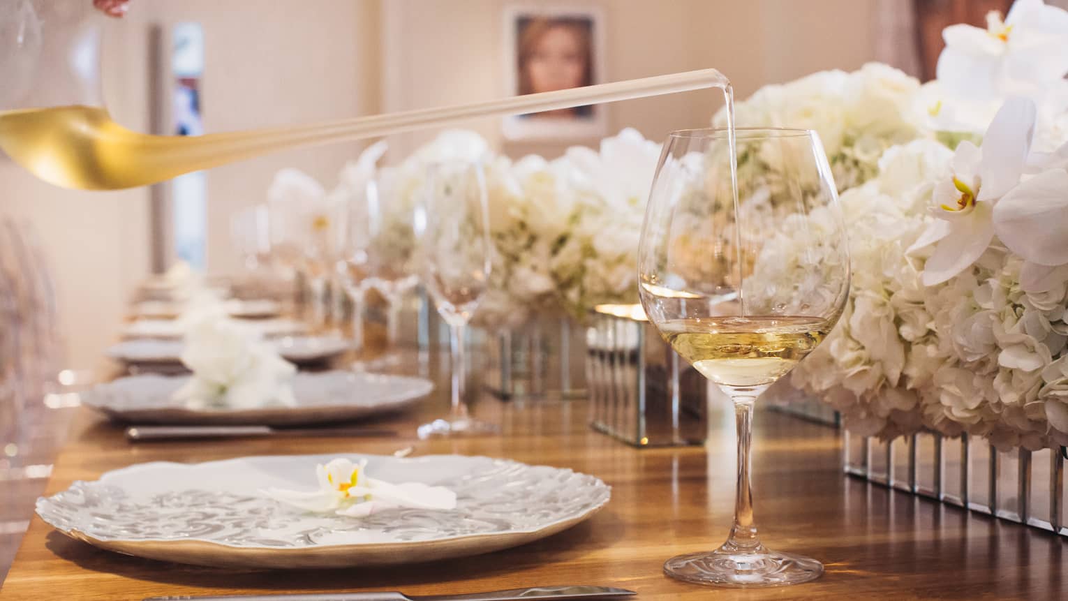 Close-up of glass of white wine, white roses along formal banquet table