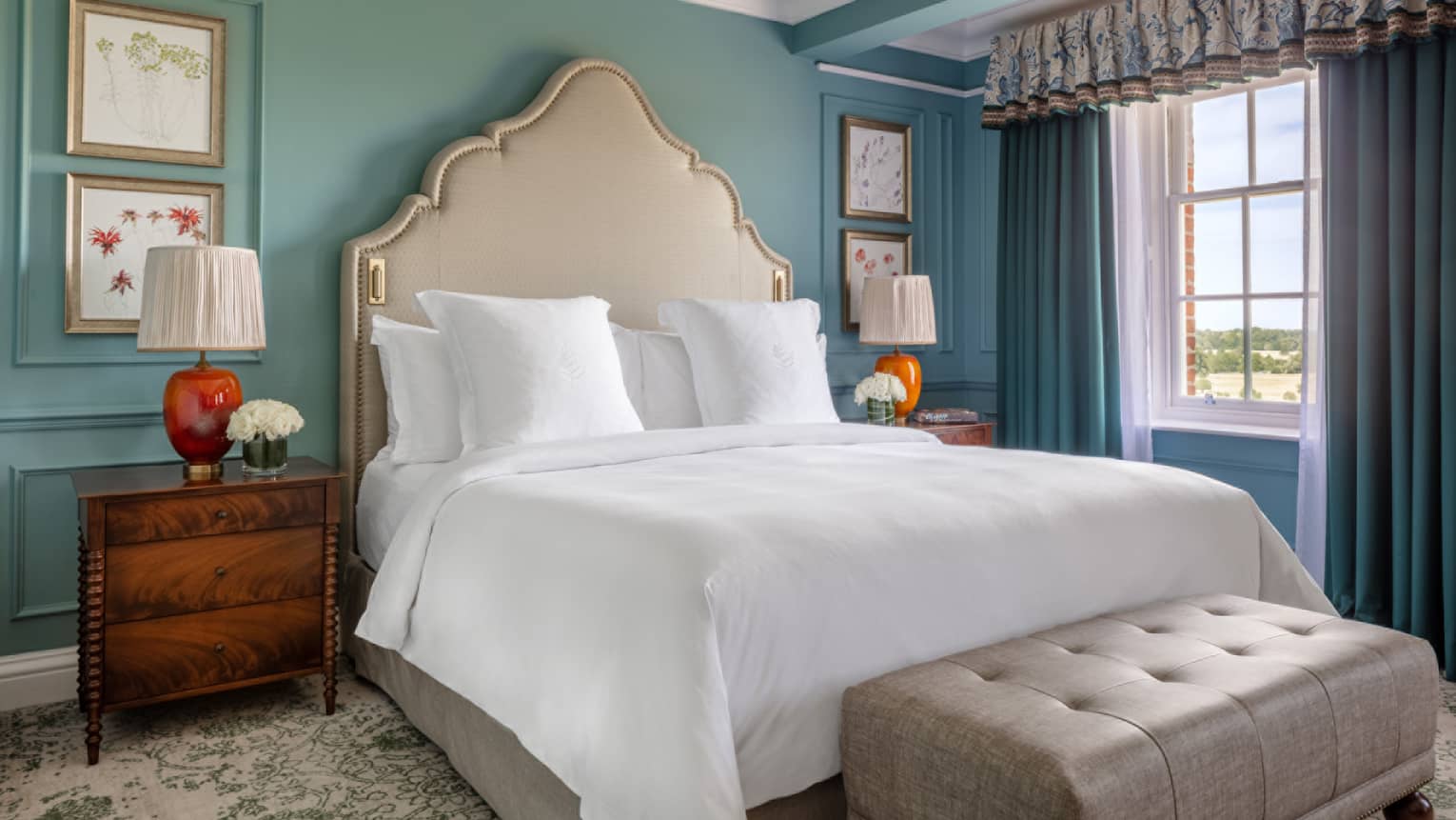 Guest room with Queen bed, cream headboard, cherry bed side table, window with blue drapes