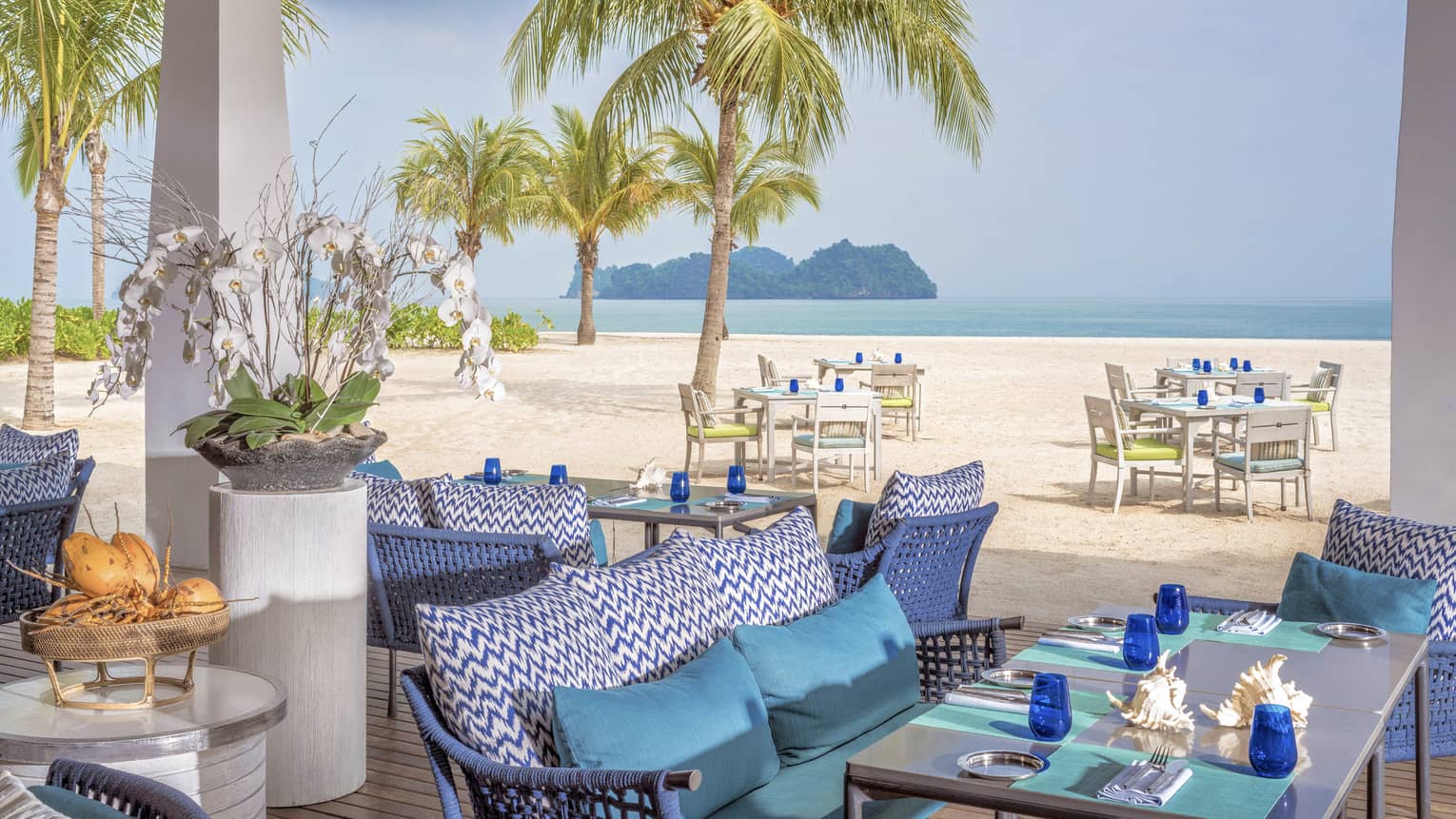 Terrace of ocean-view restaurant, blue cushions on sofa, turquoise place mats and blue glasses on table