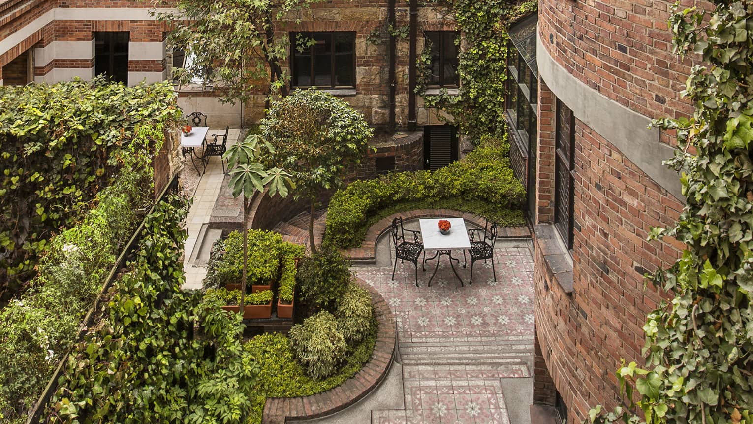 Aerial view of wrought-iron patio tables and chairs in brick courtyard, trees and shrubs throughout