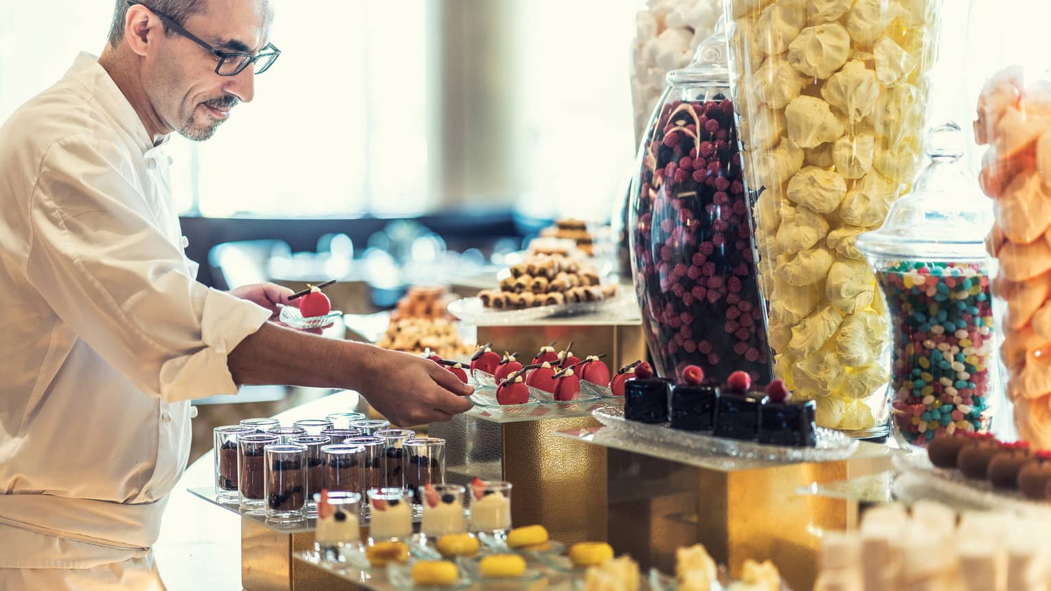 A chef prepares several chocolate pastries inside a patisserie. 