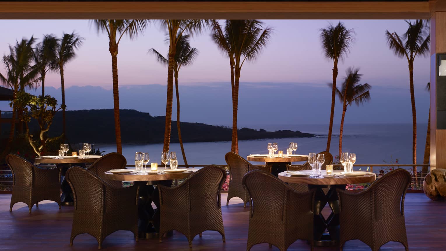 Wicker dining chairs around patio tables overlooking beach on One Forty patio at night