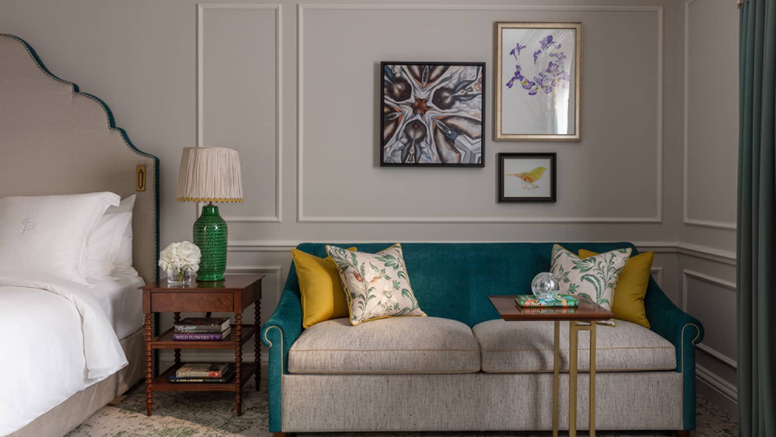 Cream and turquoise loveseat with mustard-coloured pillows, bedside table with green lamp, trio of wall art